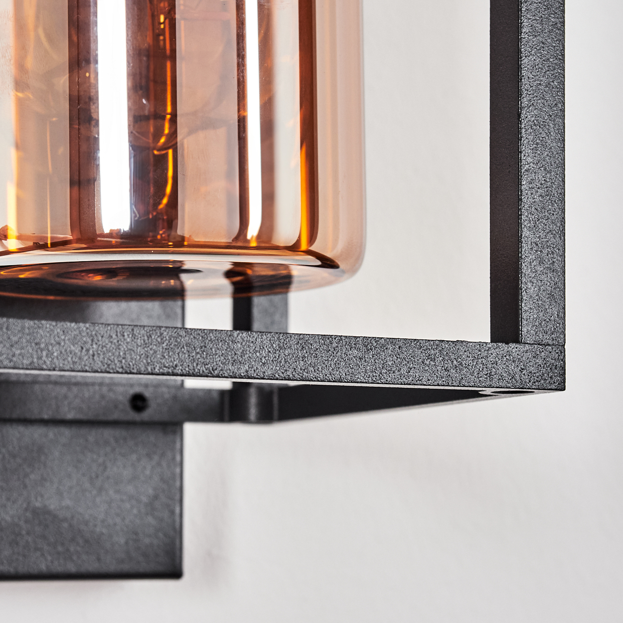 Eine Nahaufnahme einer Wandleuchte mit bernsteinfarbenem Glaszylinder und schwarzem Metallrahmen.