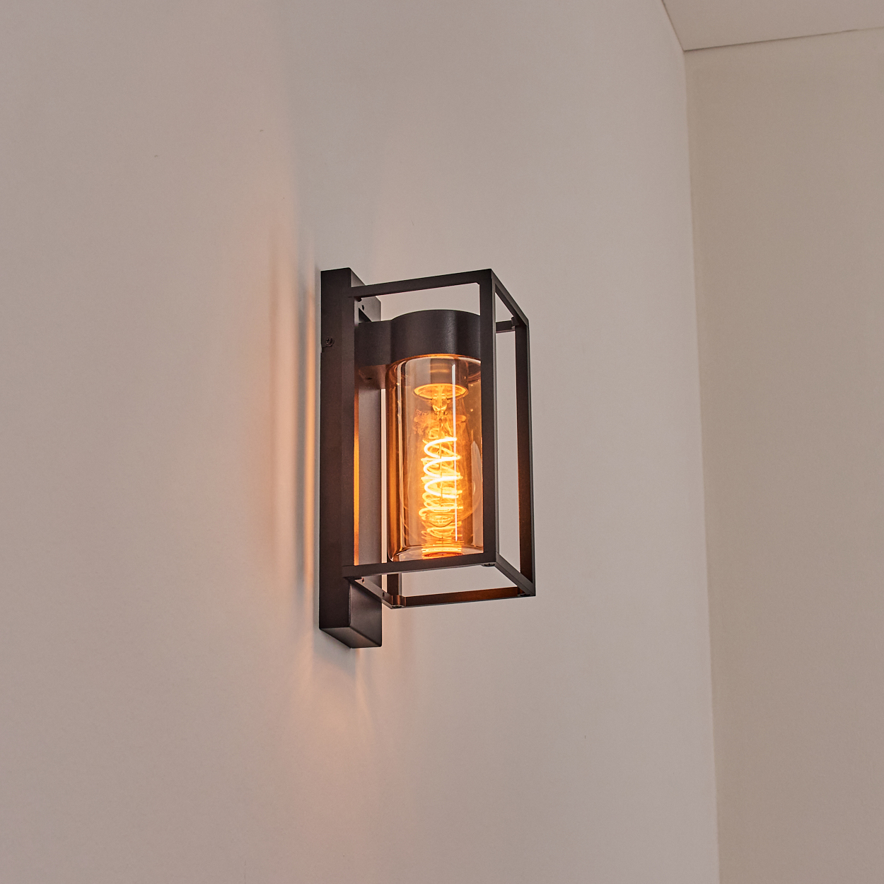 Eine schwarze Wandleuchte mit Glaskolben und Glühfadenlampe.