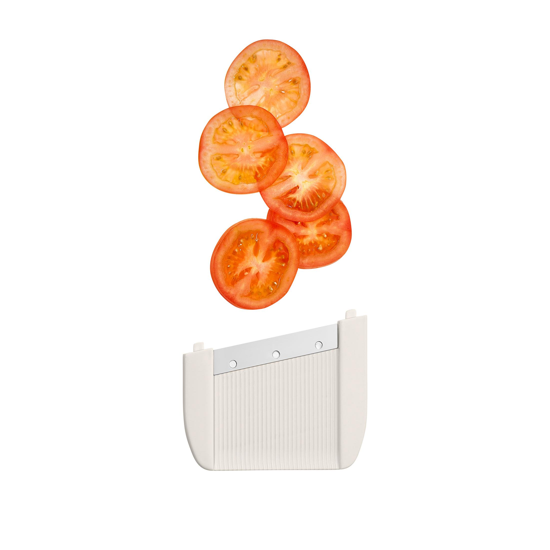 Fette di pomodoro tagliate fluttuano sopra un'affettatrice per verdure bianca.