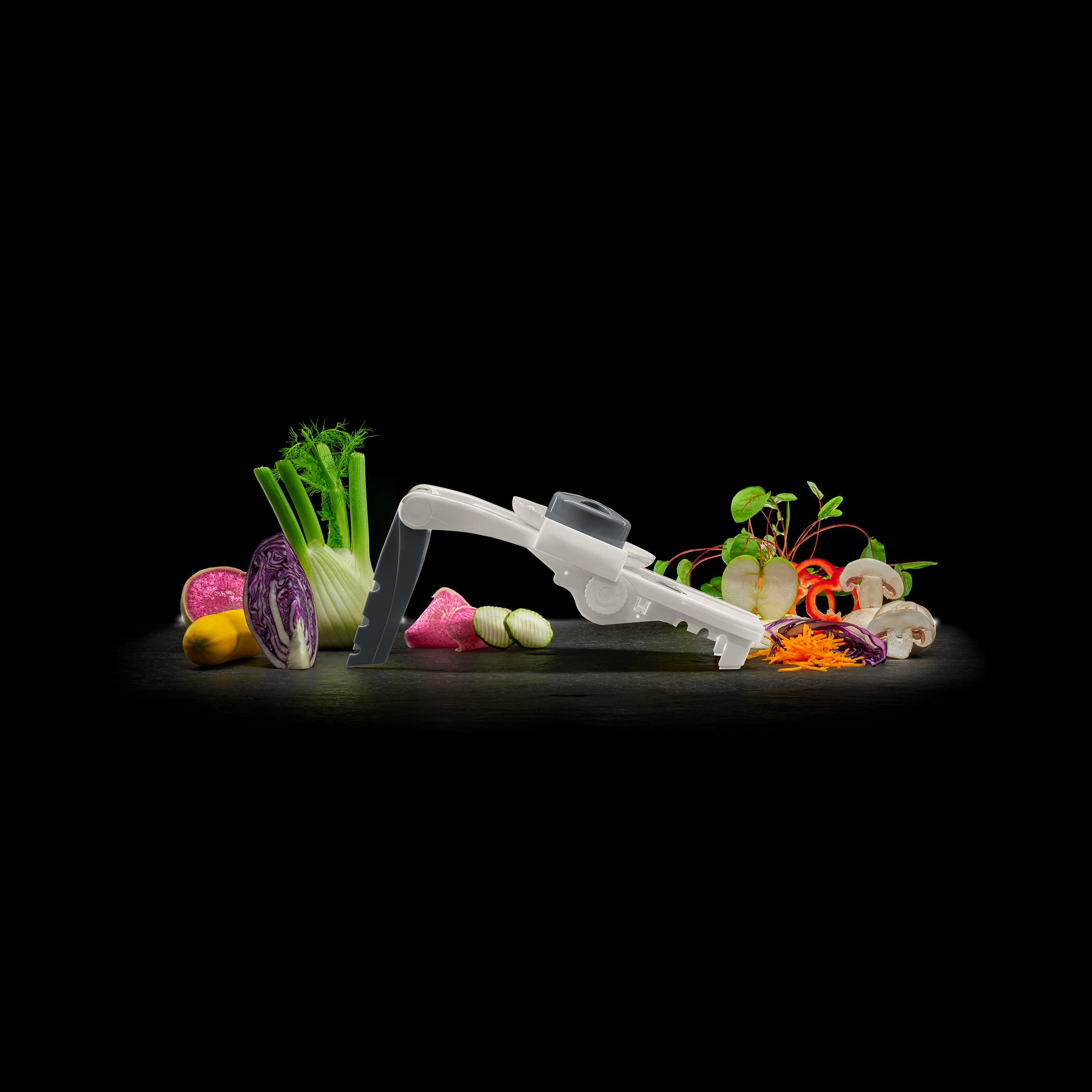Affettatrice di verdure con verdure colorate come carote, cavolo e funghi su sfondo nero.