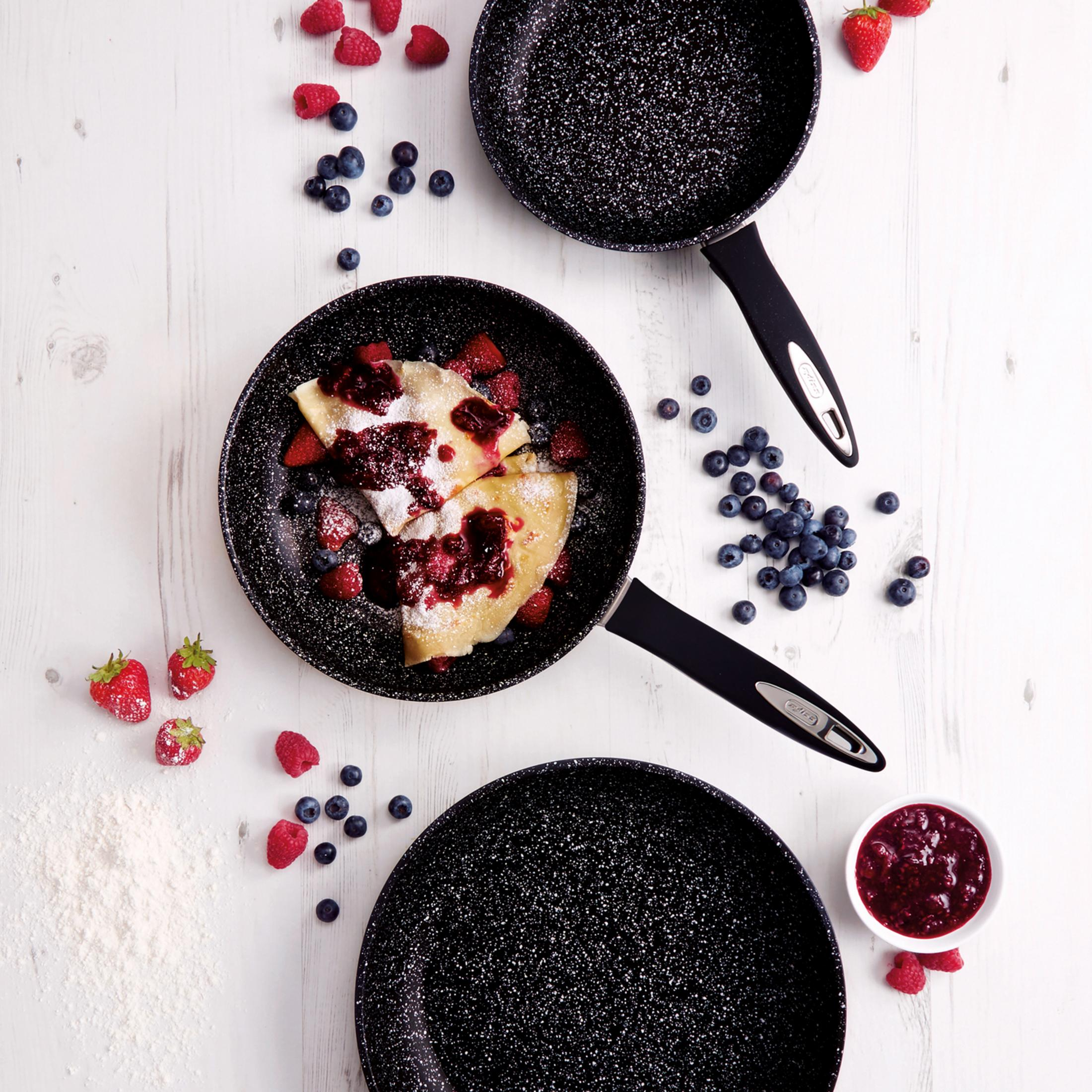 Pfannkuchen mit Beeren und Puderzucker in Pfannen auf Holzhintergrund.