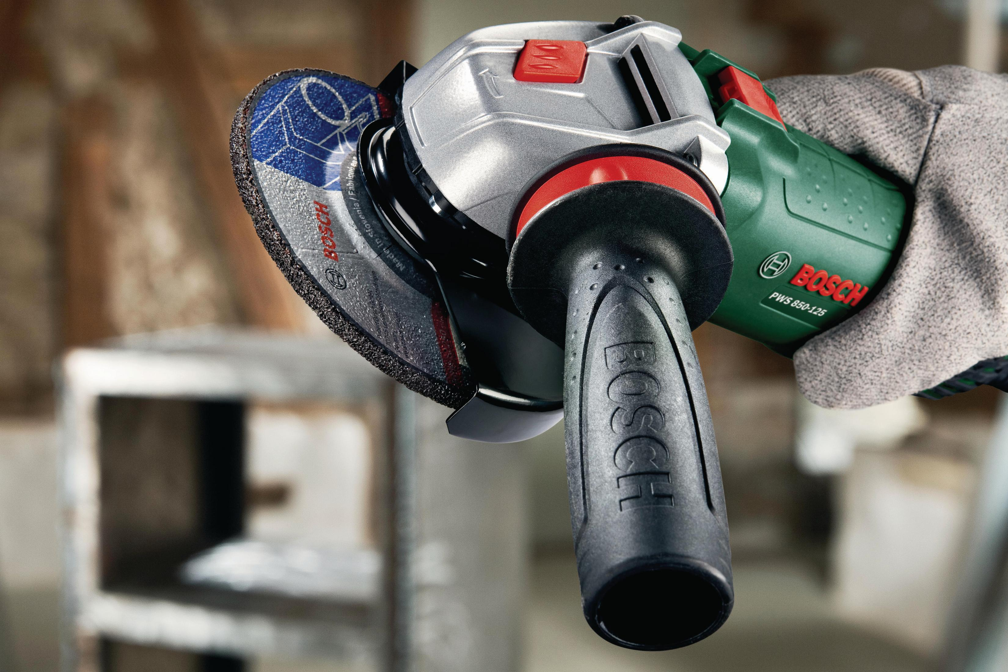 Hand hält eine Bosch Winkelschleifmaschine mit blau-weißer Scheibe im Fokus.