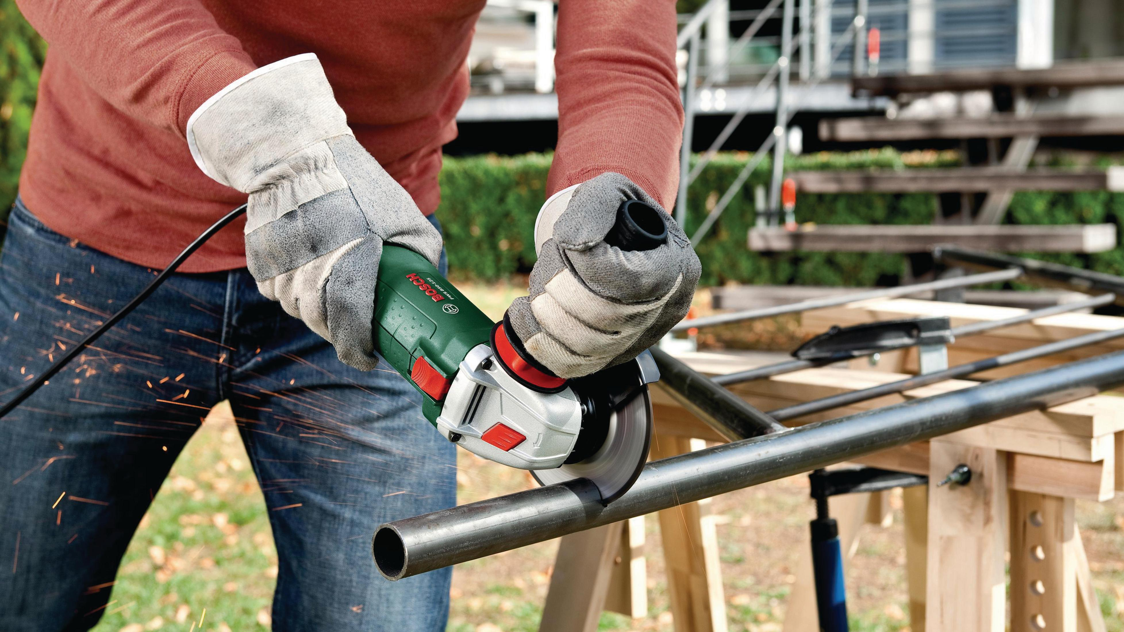 Person mit Schutzhandschuhen schneidet Metallrohr mit Winkelschleifer.
