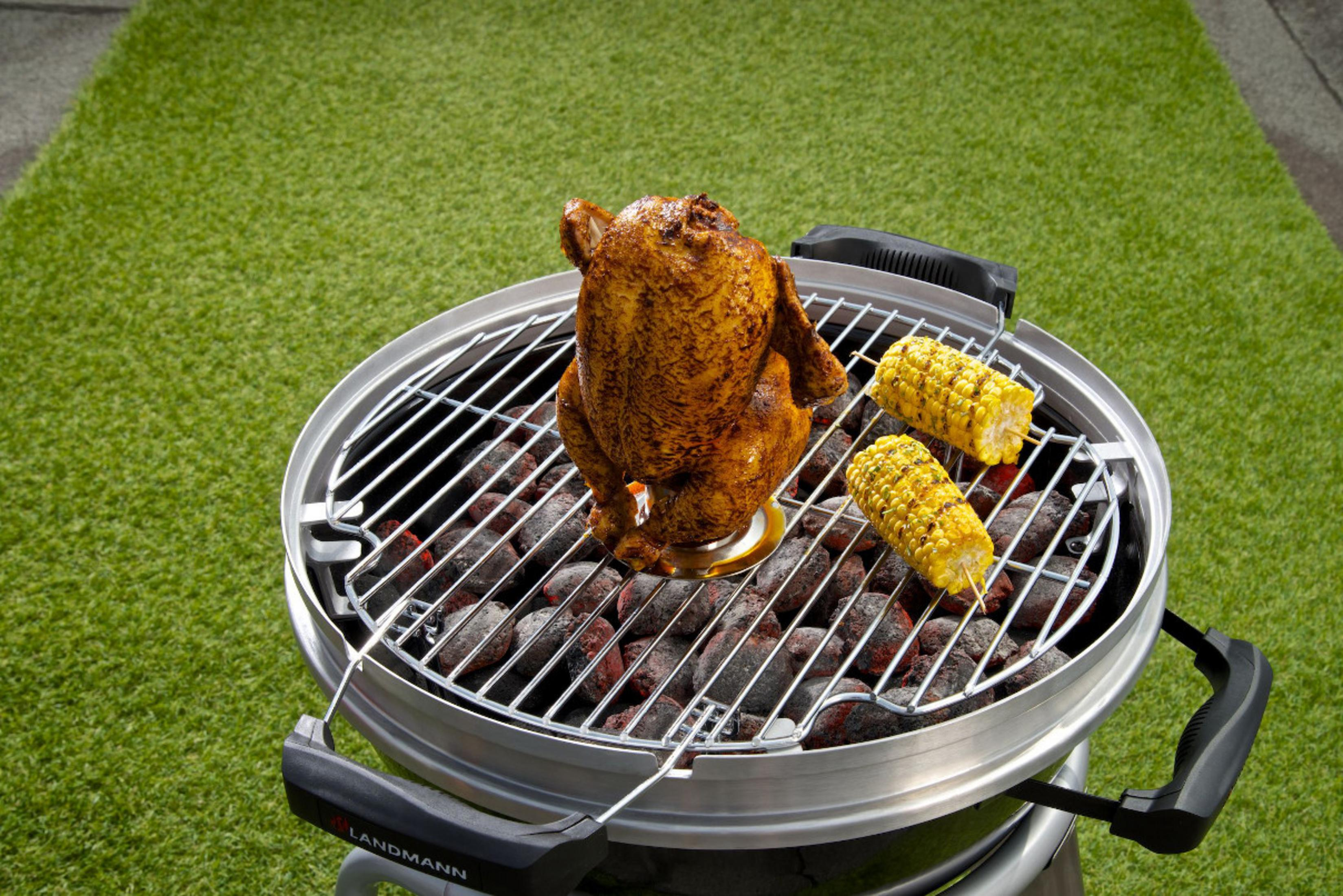 Ein gebratenes Hähnchen und Maiskolben auf einem Grill über glühender Kohle.