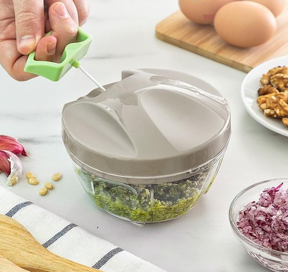 Un tritatutto manuale con manico verde, riempito di purea verde tritata.