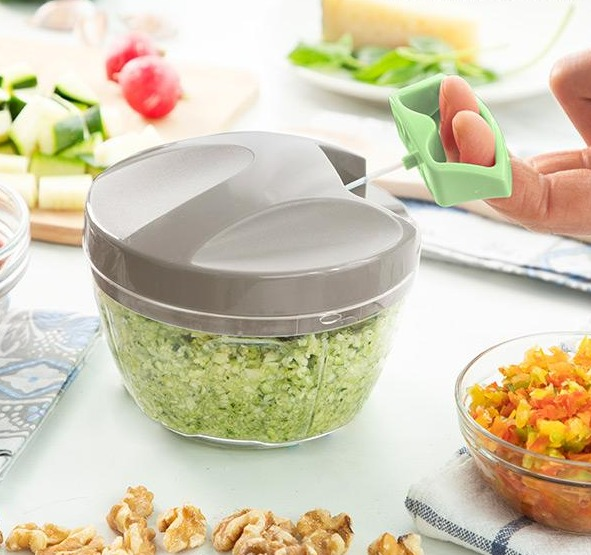 Un tritatutto manuale con coperchio grigio, riempito di verdure verdi tritate.