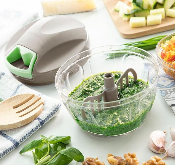 Un tritatutto con pesto verde nella sua ciotola, accanto a basilico, noci e aglio.