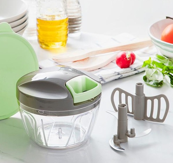 Un tritatutto manuale con contenitore trasparente, coperchio grigio e accenti verdi.