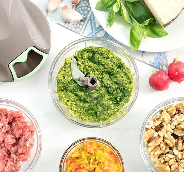 Tritatutto con ciotola di pesto, carne macinata, noci e verdure tritate.