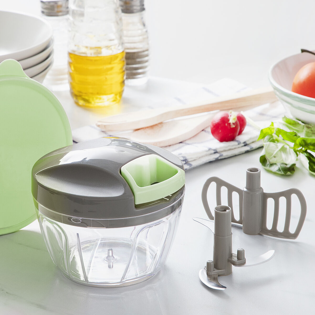 Un tritatutto da cucina trasparente con coperchio grigio e dettagli verdi vicino alle lame.