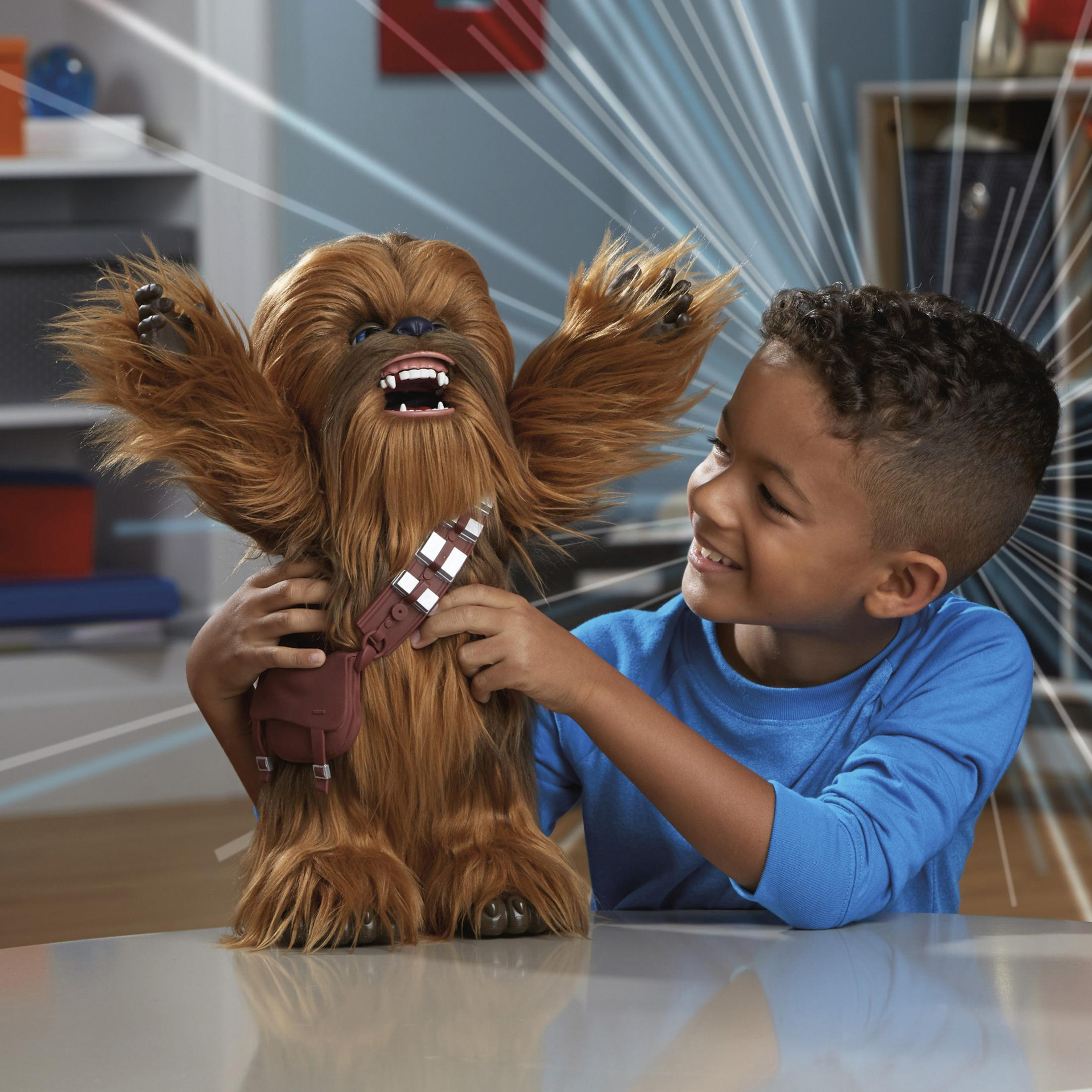 Un bambino con maglia blu sorride tenendo un giocattolo di Chewbacca con le braccia alzate.