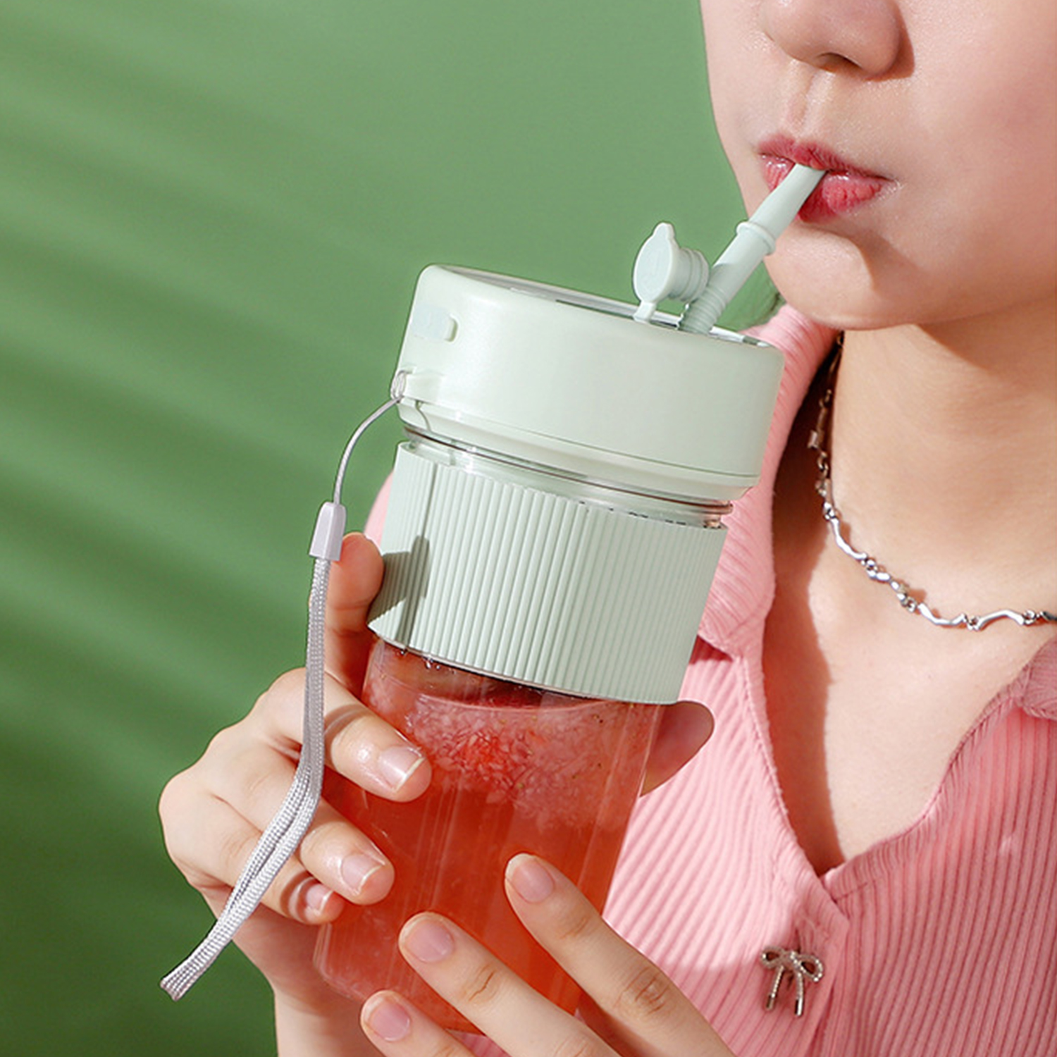 Persona beve da una tazza verde chiaro con cannuccia.