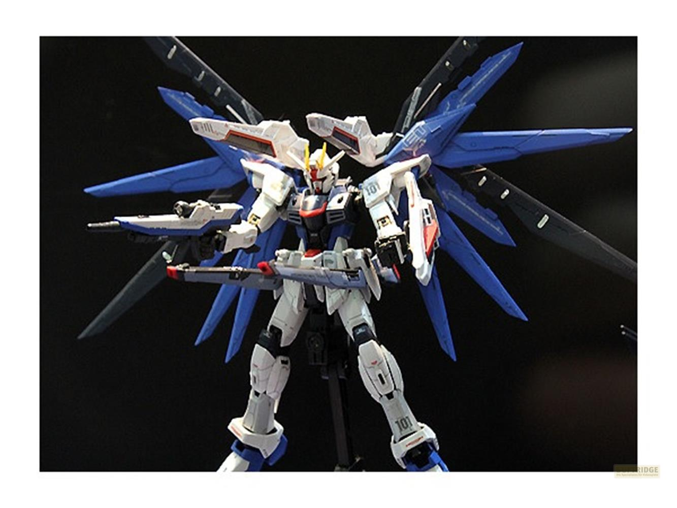 Ein weißer und blauer Gundam-Roboter mit großen blauen Flügeln auf schwarzem Hintergrund.
