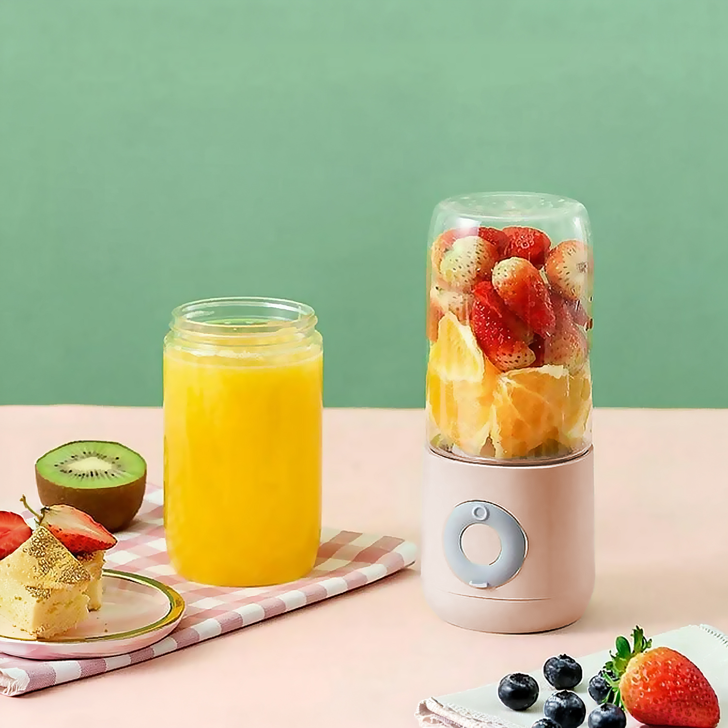 Un frullatore con frutta, succo e torta su sfondo rosa e verde.