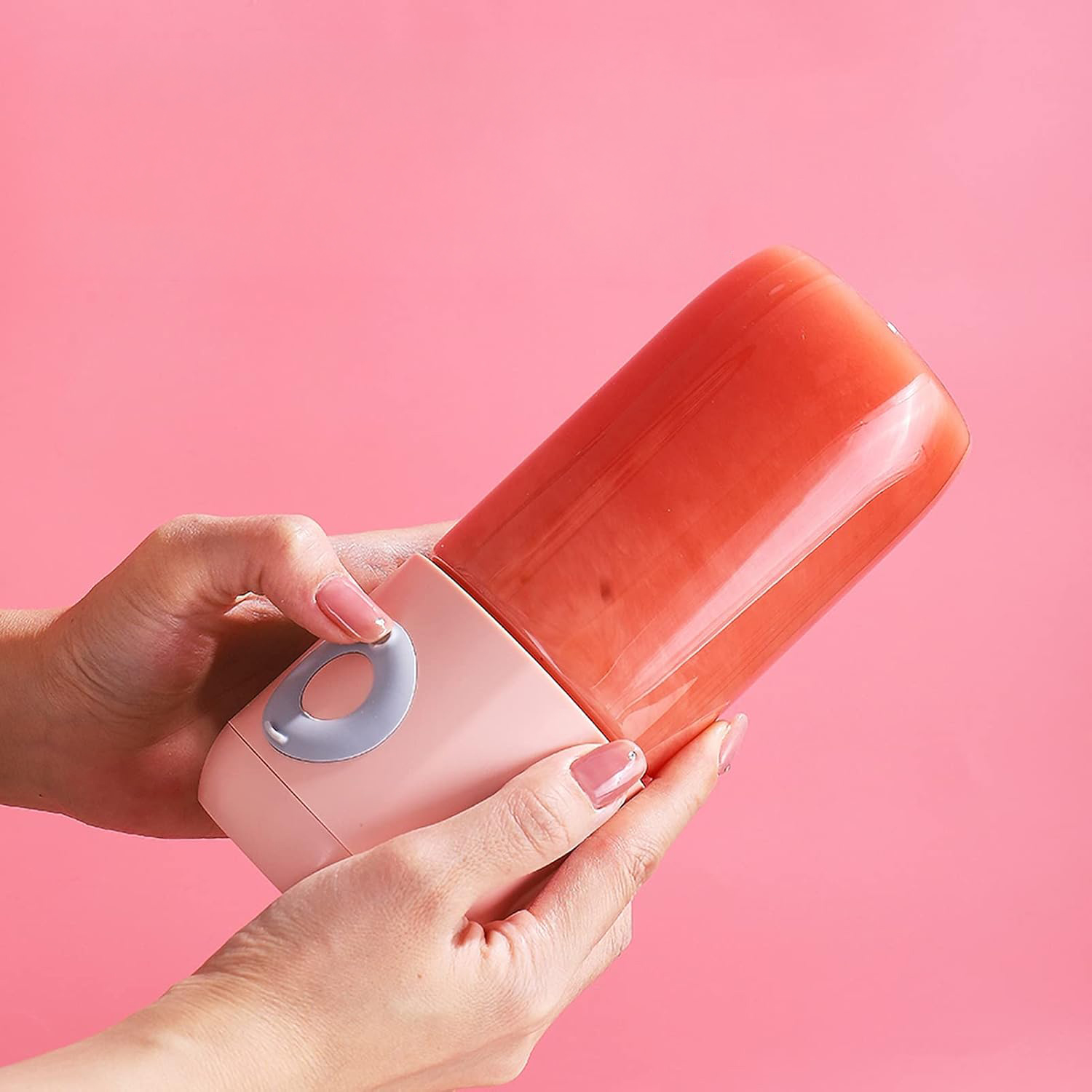 Mani che tengono un frullatore rosa con succo rosso su sfondo rosa.