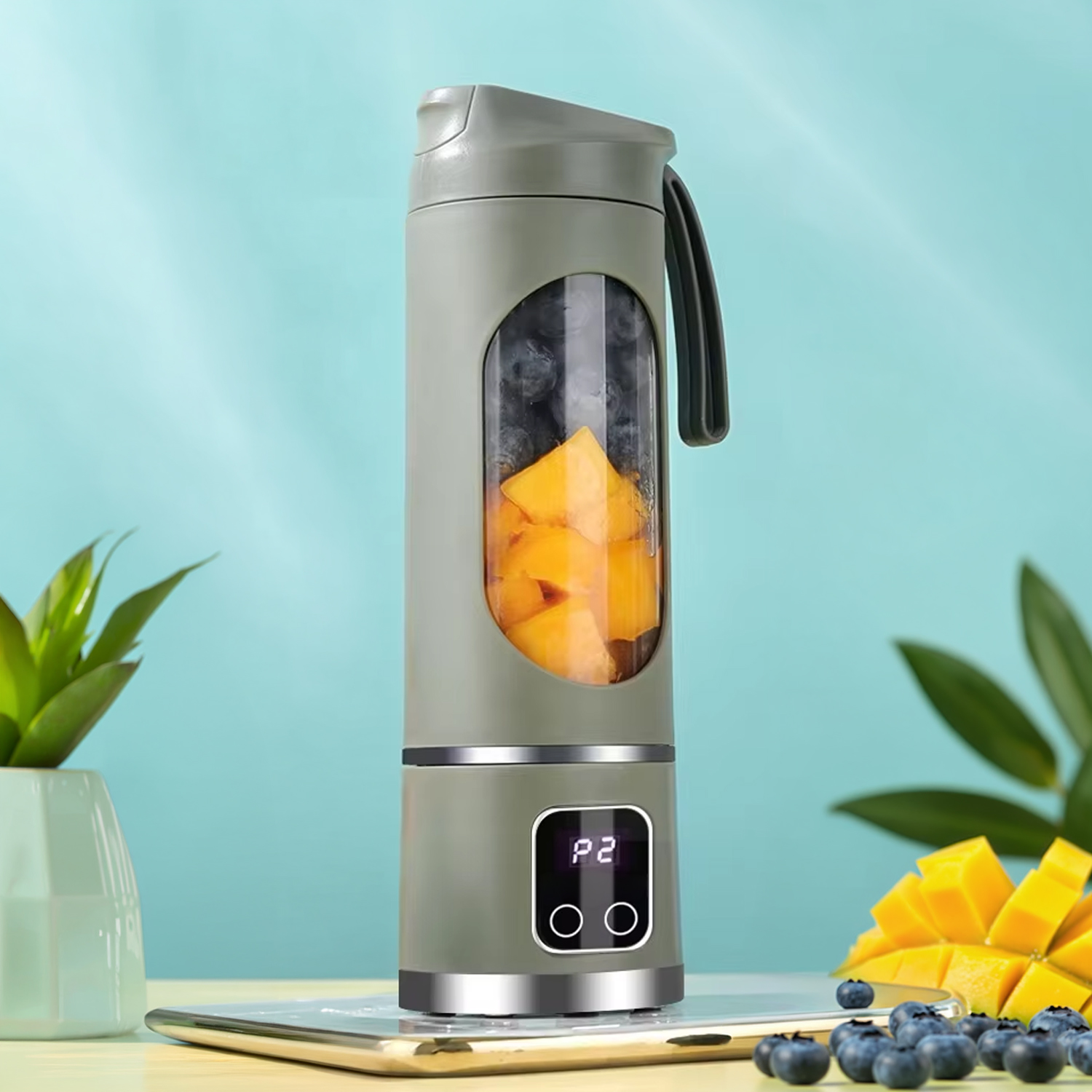 Frullatore grigio con pezzi di frutta e mirtilli, accanto a cubetti di mango e una pianta.
