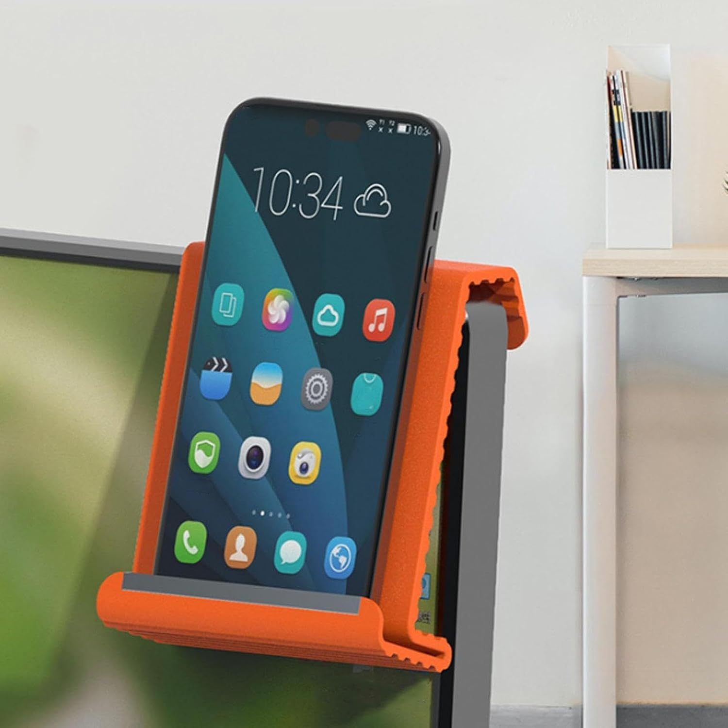 Ein Smartphone mit Apps wird in einem orangefarbenen Ständer gehalten. Es ist 10:34 Uhr.