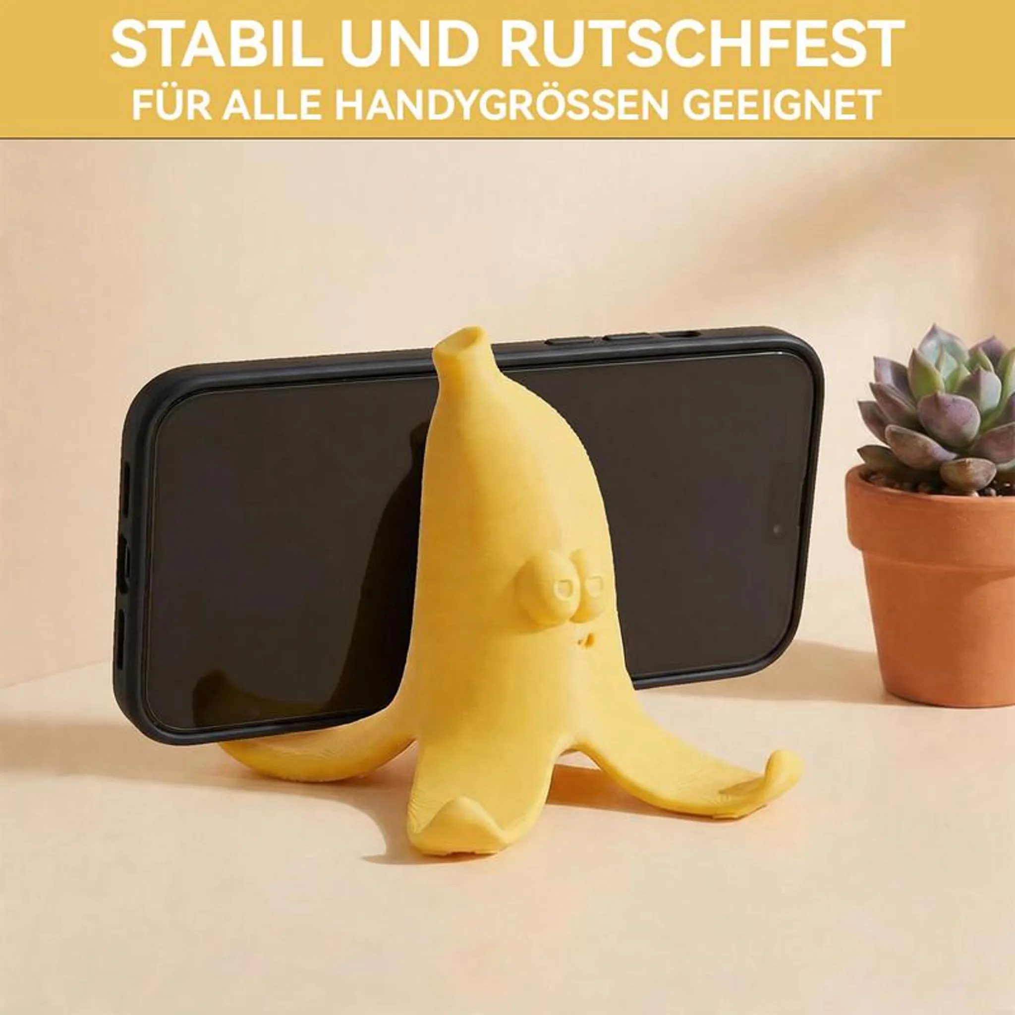 Ein gelber Bananen-Handyständer hält ein schwarzes Smartphone. Rechts steht eine Sukkulente.