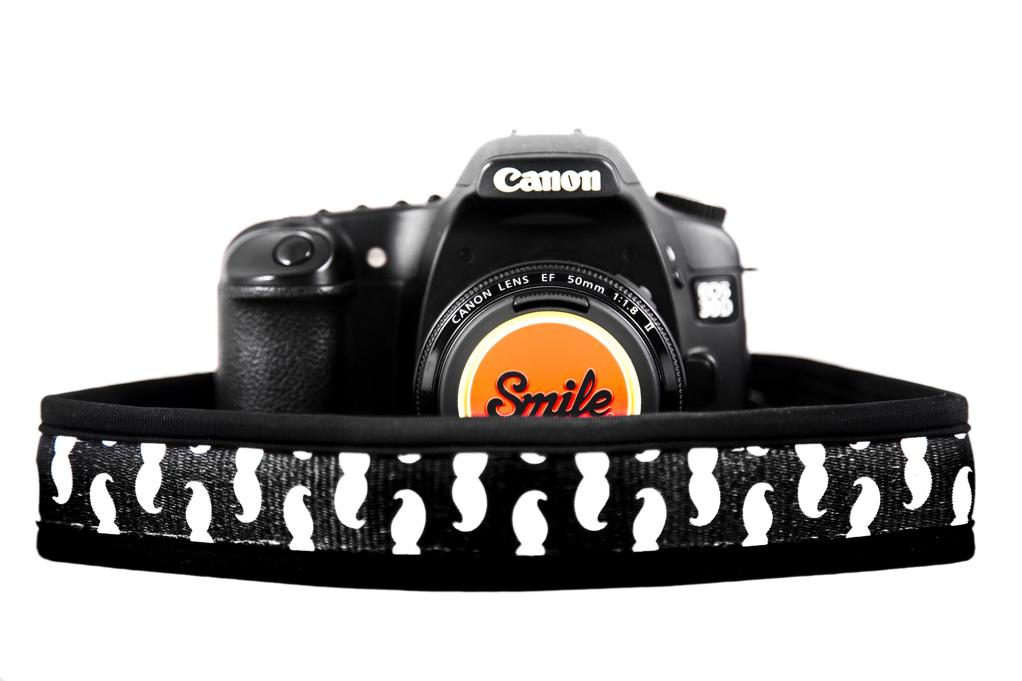 Una fotocamera Canon nera con tappo obiettivo "Smile" e tracolla con pinguini.