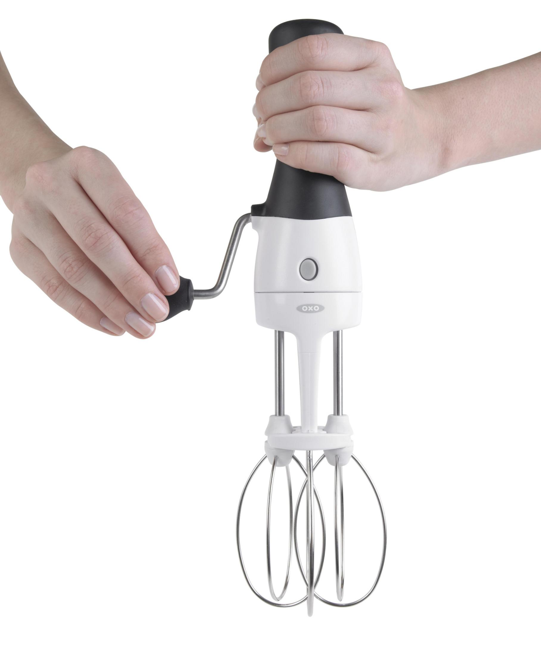 Eine Hand kurbelt einen weißen Handmixer mit schwarzem Griff und silbernen Quirlen.