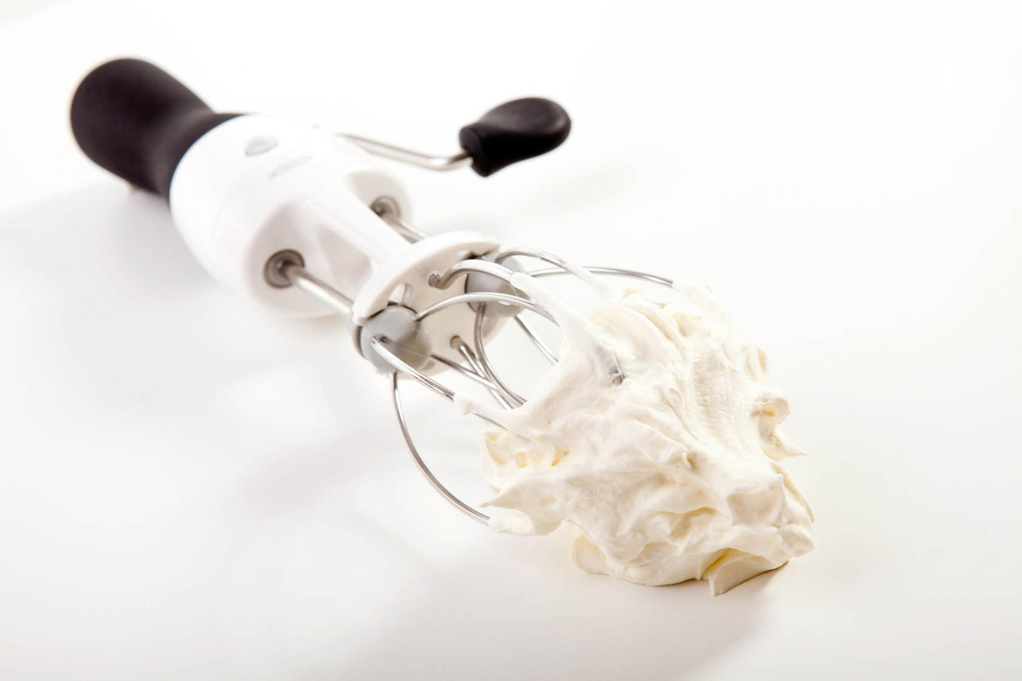 Ein weißer Handmixer mit schwarzem Griff, der Schlagsahne aufwirbelt.