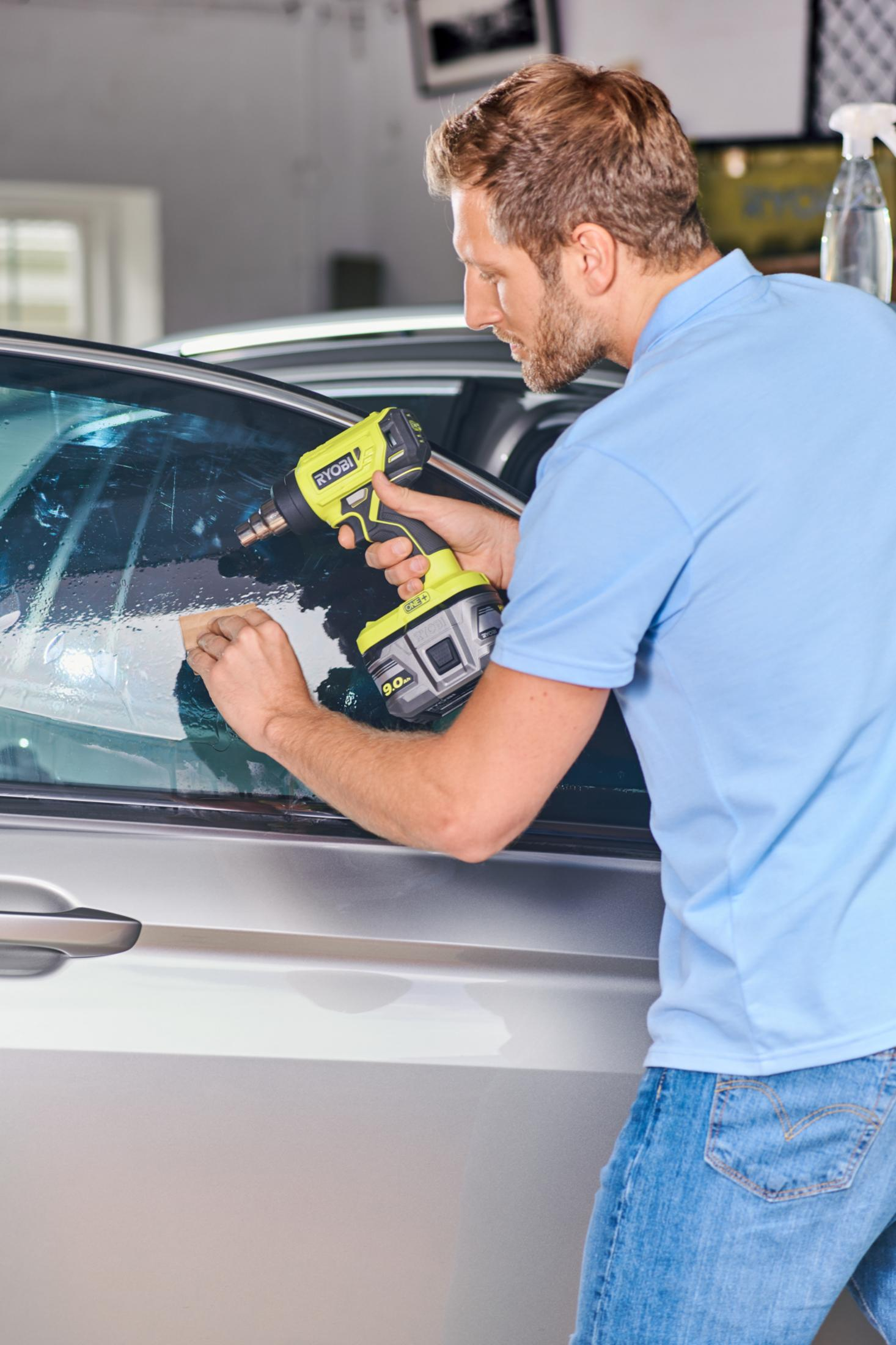 Uomo usa pistola termica e panno per applicare tinta a finestrino auto.