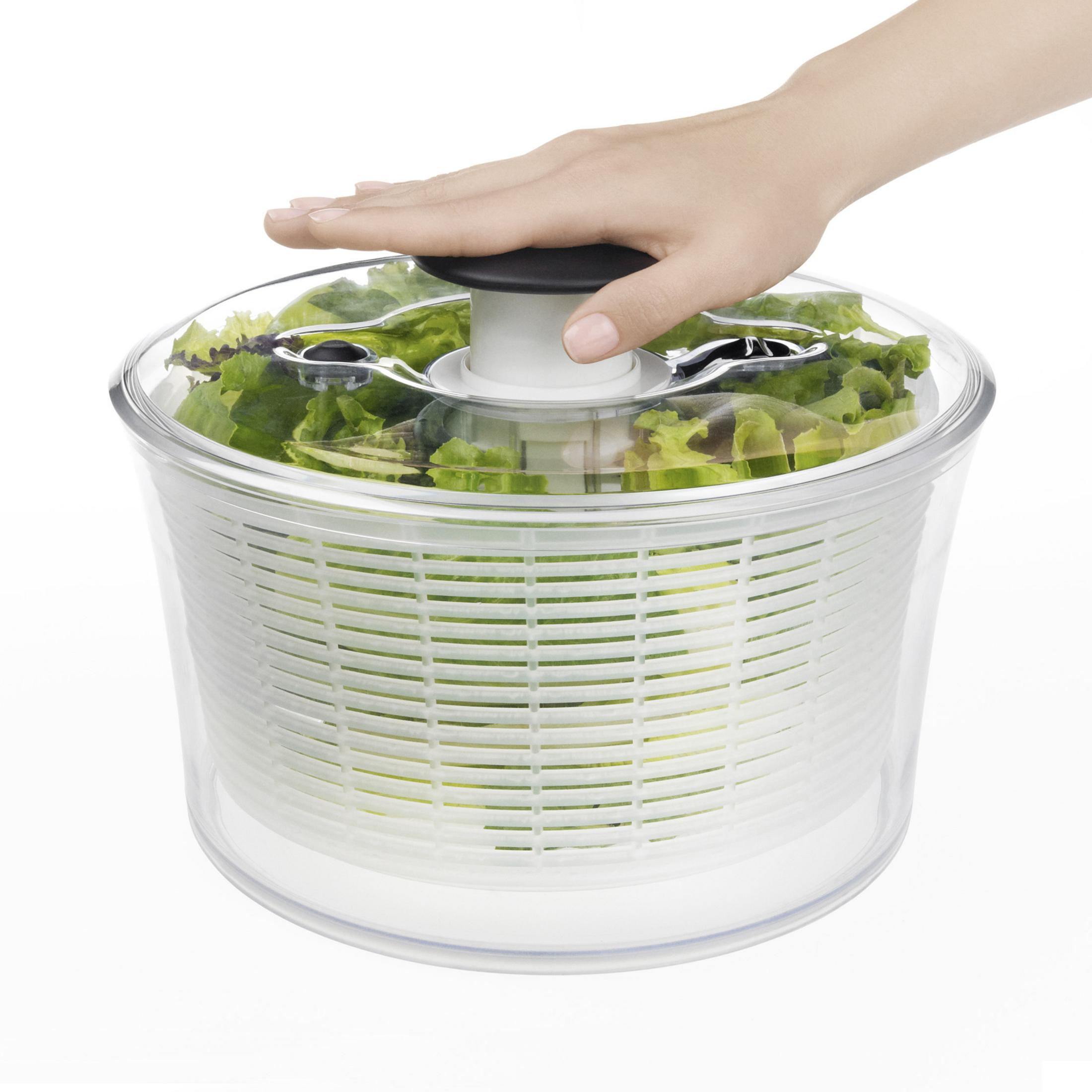 Hand drückt auf Salat-Schleuder mit grünem Salat.