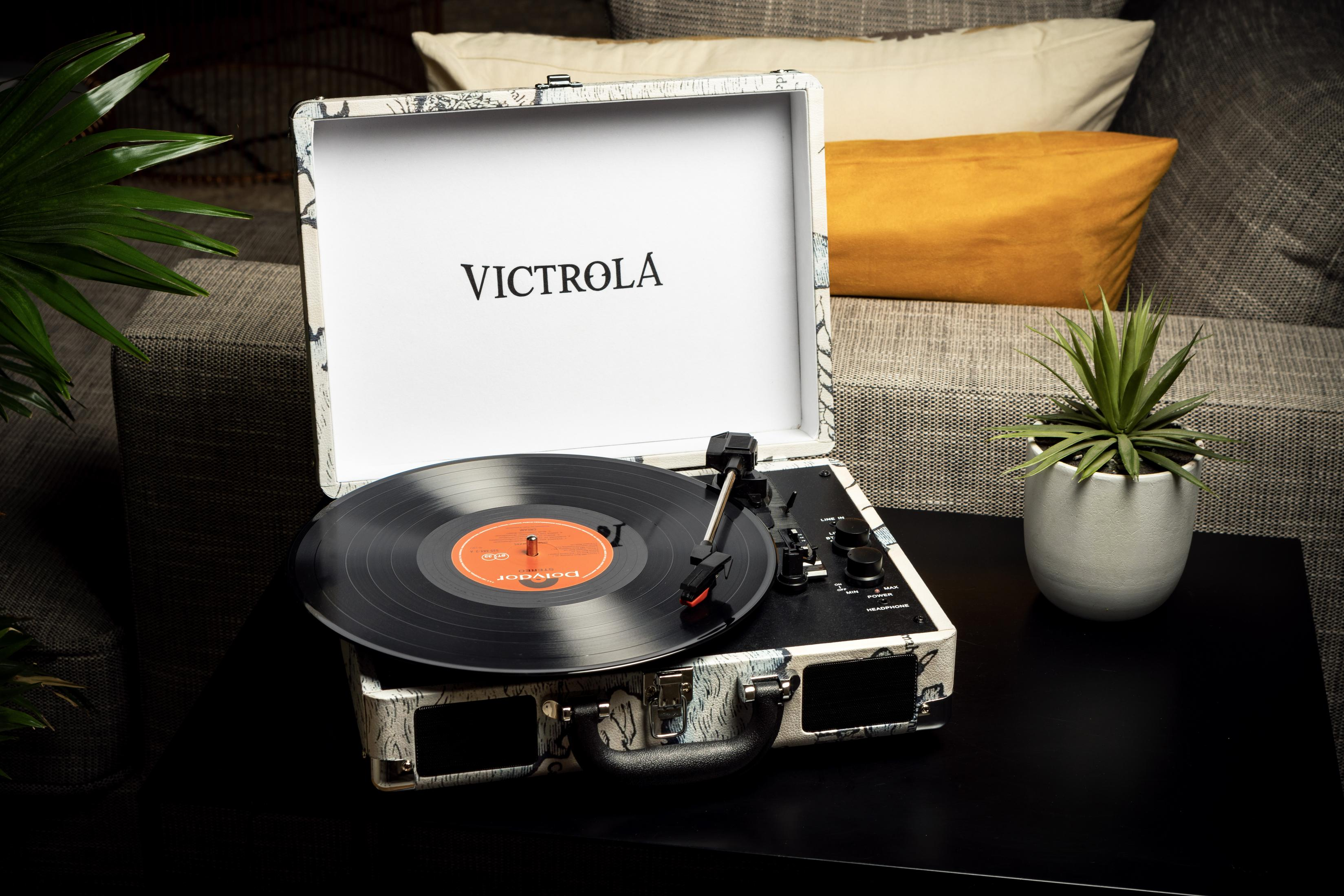 Un tocadiscos Victrola con un disco de vinilo y una planta verde en maceta.