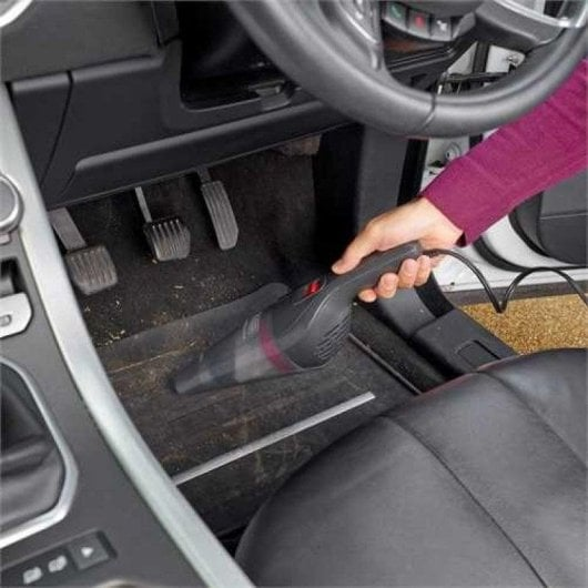 Una mano usa un aspirapolvere portatile nero sui tappetini sporchi dell'auto.