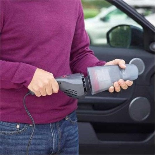 Uomo tiene aspirapolvere auto e contenitore accanto alla portiera.