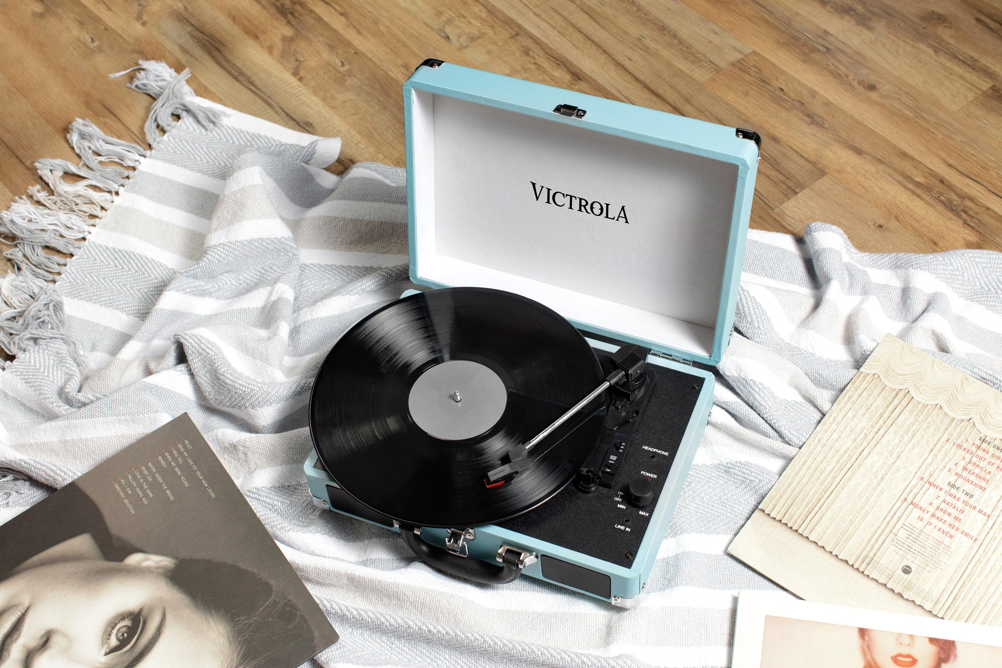 Un giradischi azzurro con disco in vinile su una coperta su pavimento in legno.