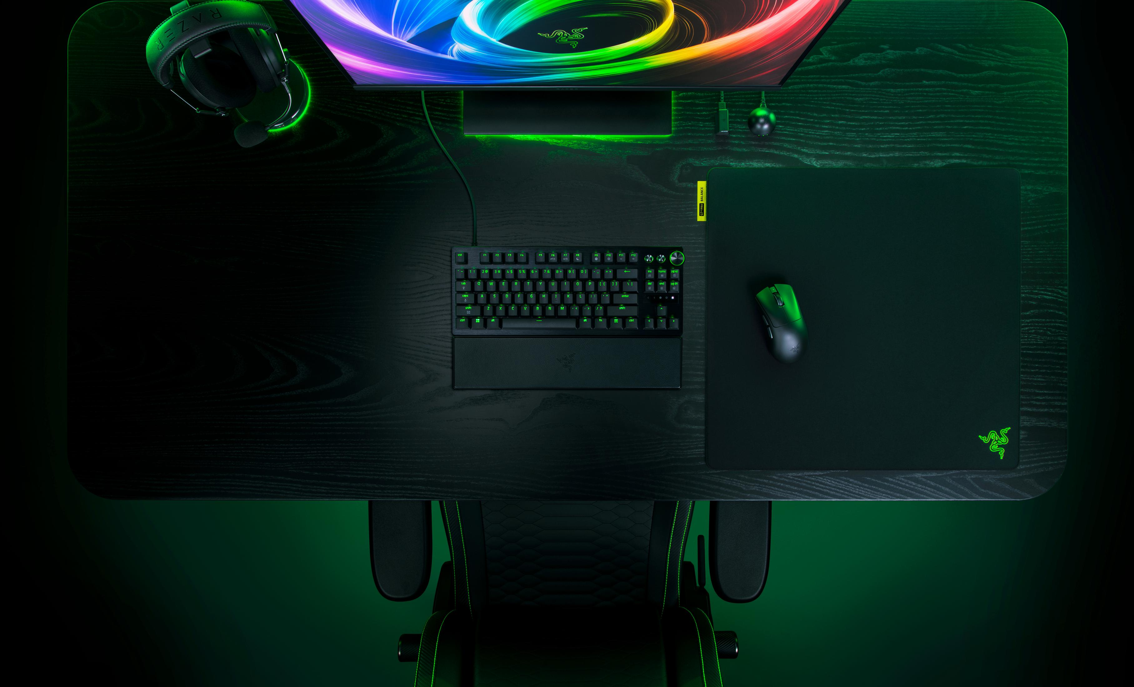 Un bureau gaming avec clavier, souris, casque et moniteur dans des tons sombres avec éclairage vert.