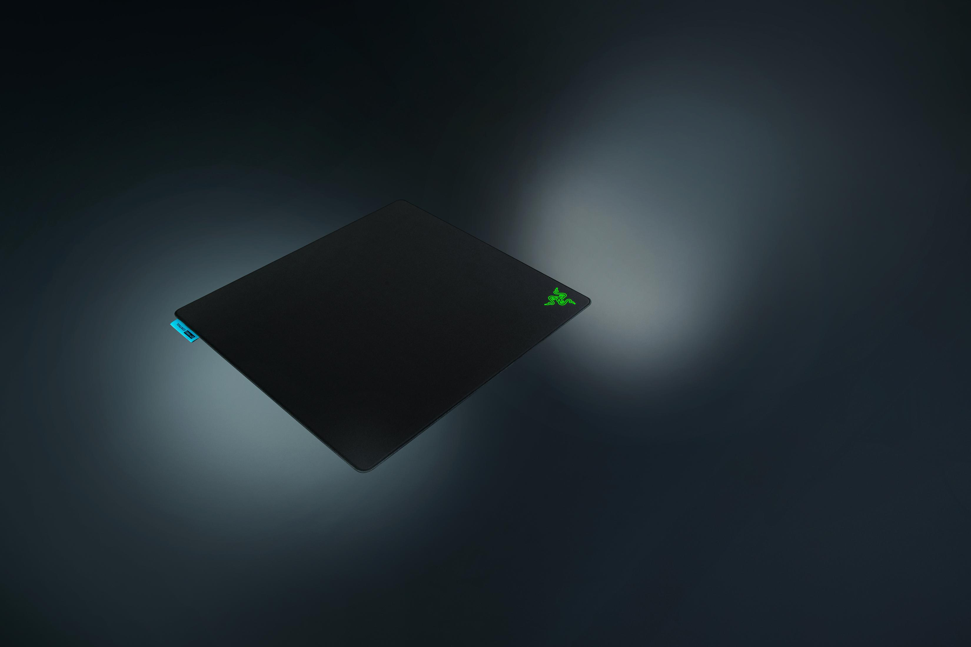 Schwarzes Mauspad mit grünem Logo und blauem Etikett auf dunklem Hintergrund.