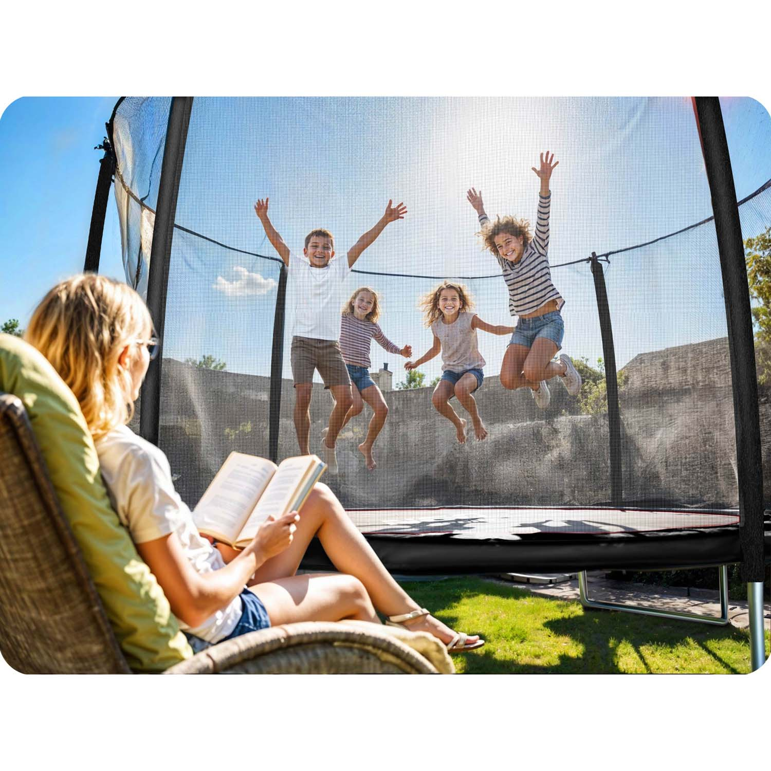 Kobieta czyta książkę w fotelu, dzieci skaczą na trampolinie w ogrodzie.