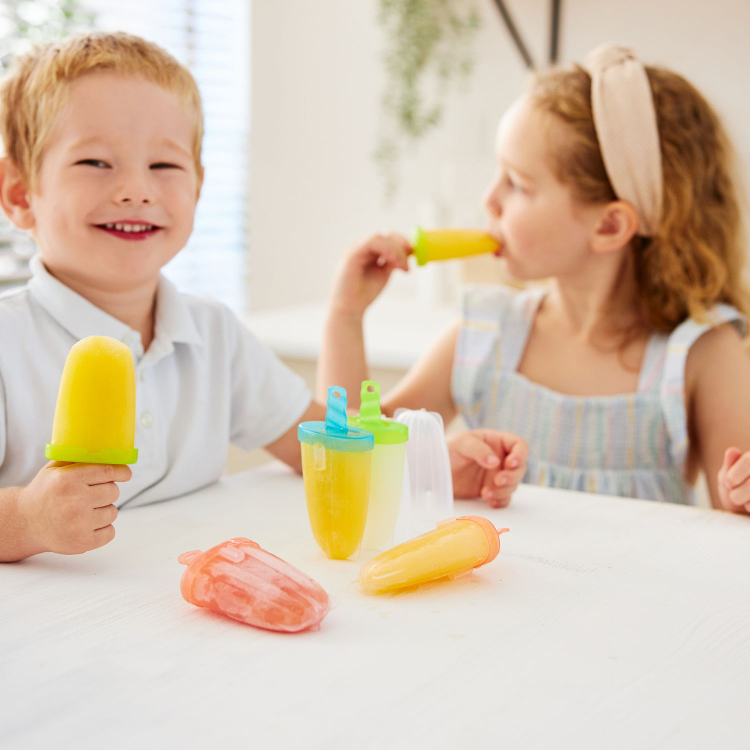 Due bambini mangiano ghiaccioli. Un bambino tiene un ghiacciolo giallo, una bambina mangia un ghiacciolo giallo.