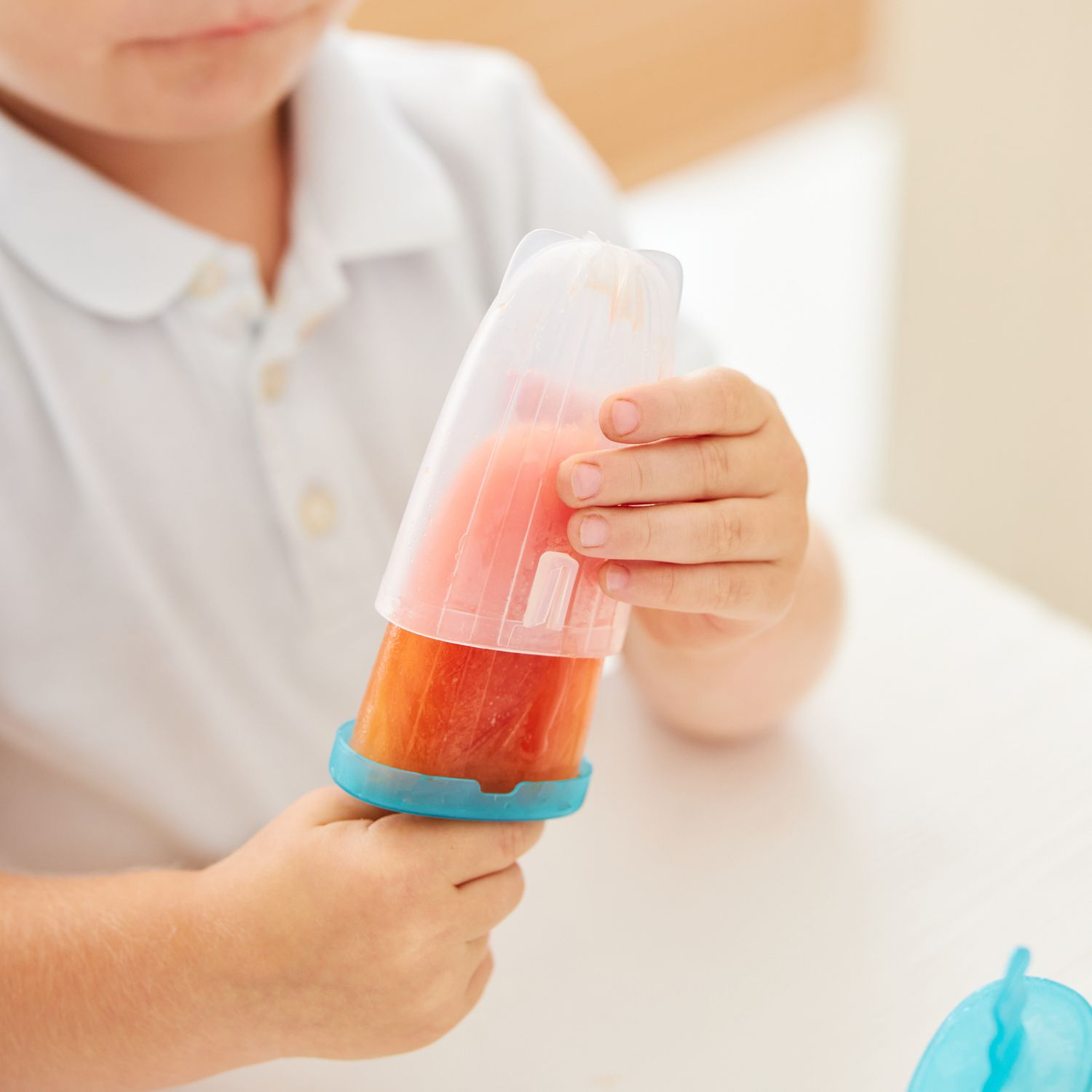 Un bambino tiene un ghiacciolo in un contenitore trasparente con manico blu.