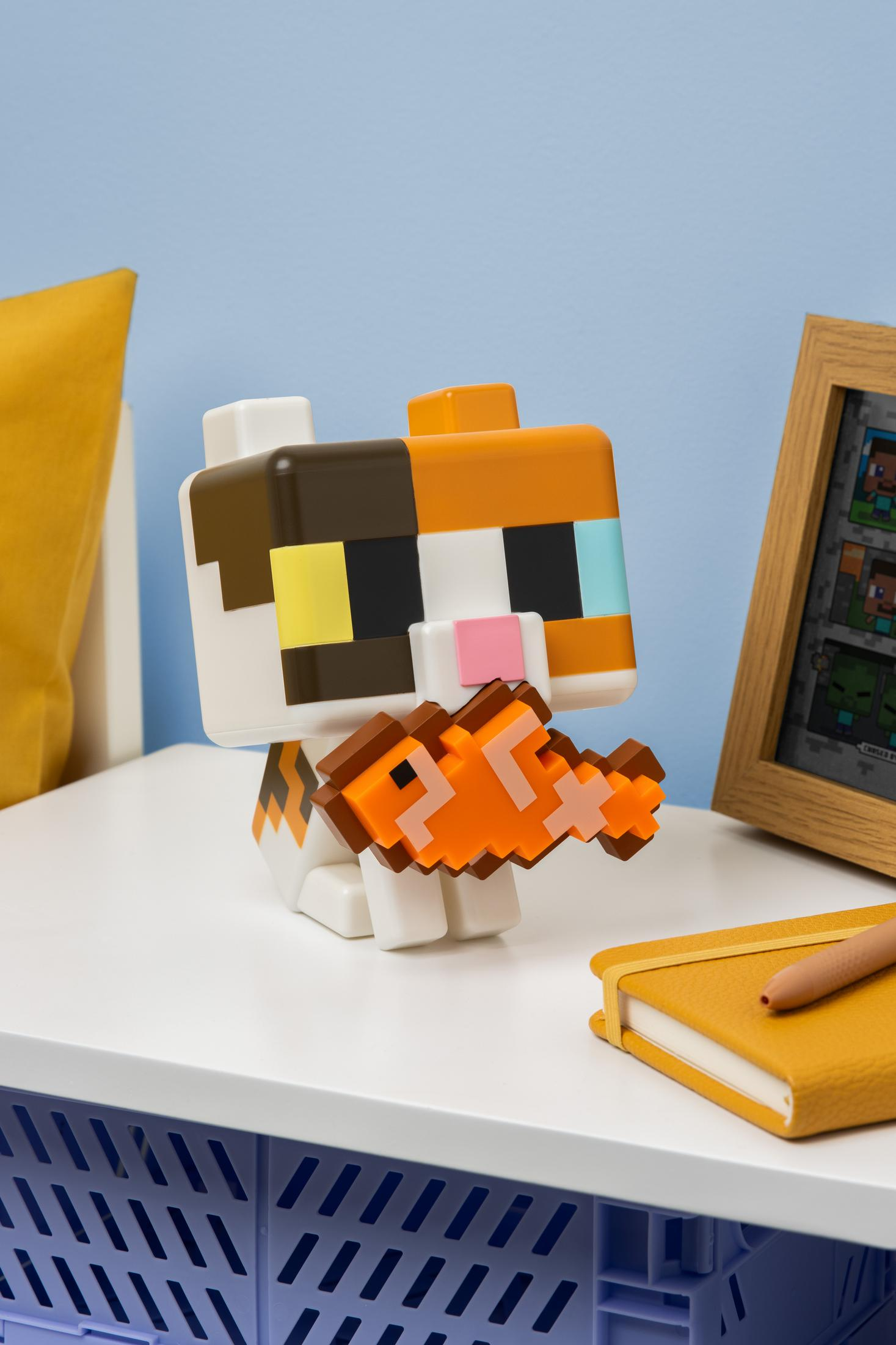 Pikselowy kot trzyma pikselową rybę, obok notatnik i ramka.