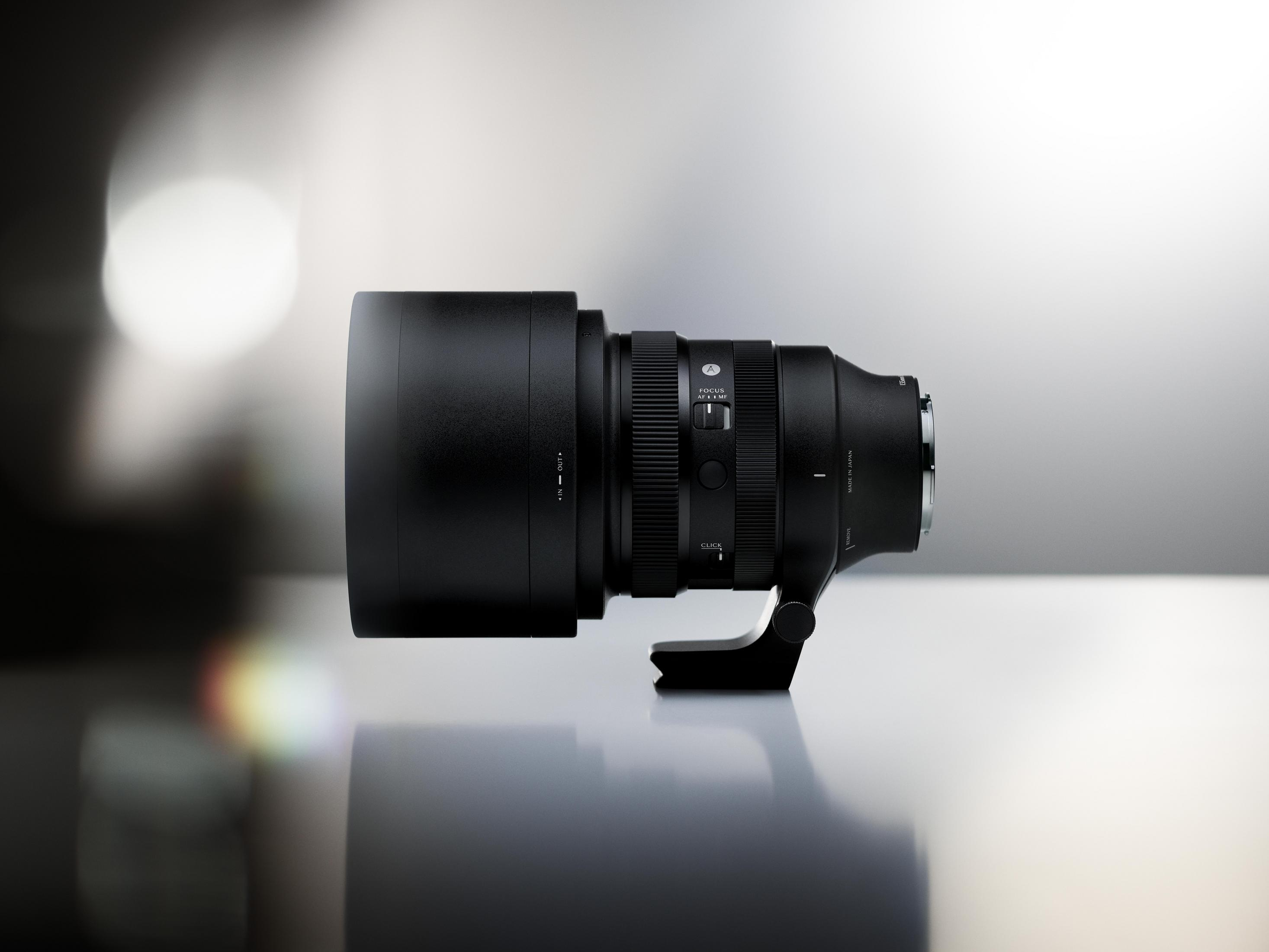 Un obiettivo per fotocamera nero con paraluce e attacco per treppiede su una superficie riflettente.
