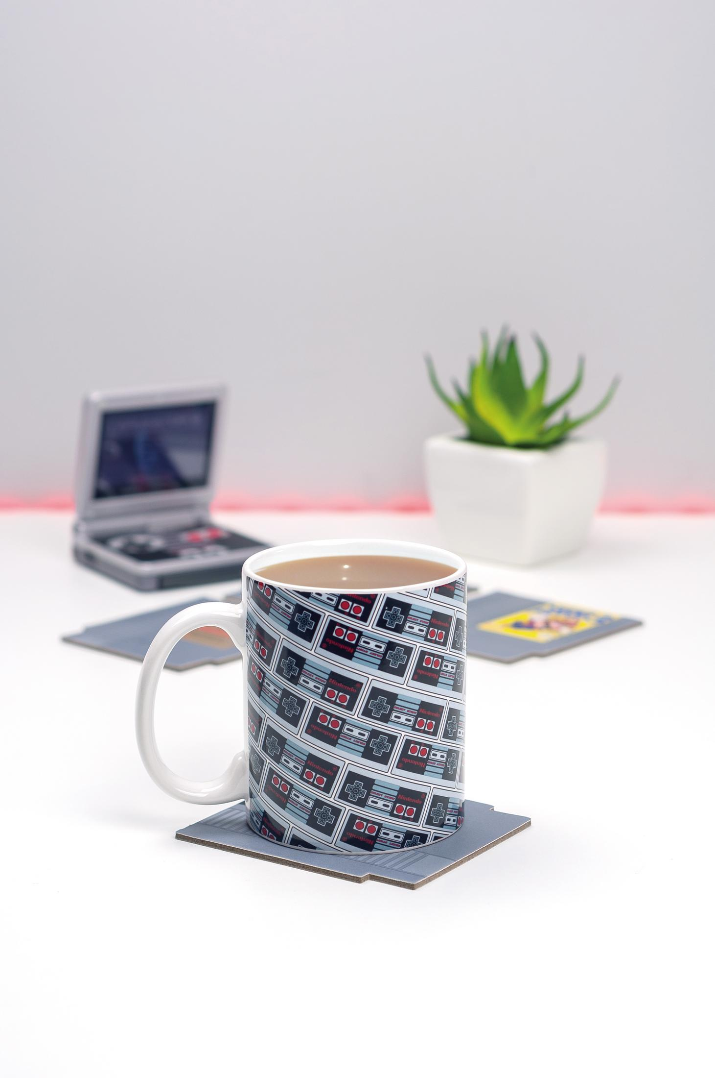 Eine Kaffeetasse mit Controller-Muster auf einem Untersetzer, daneben ein Handheld-Spielgerät.