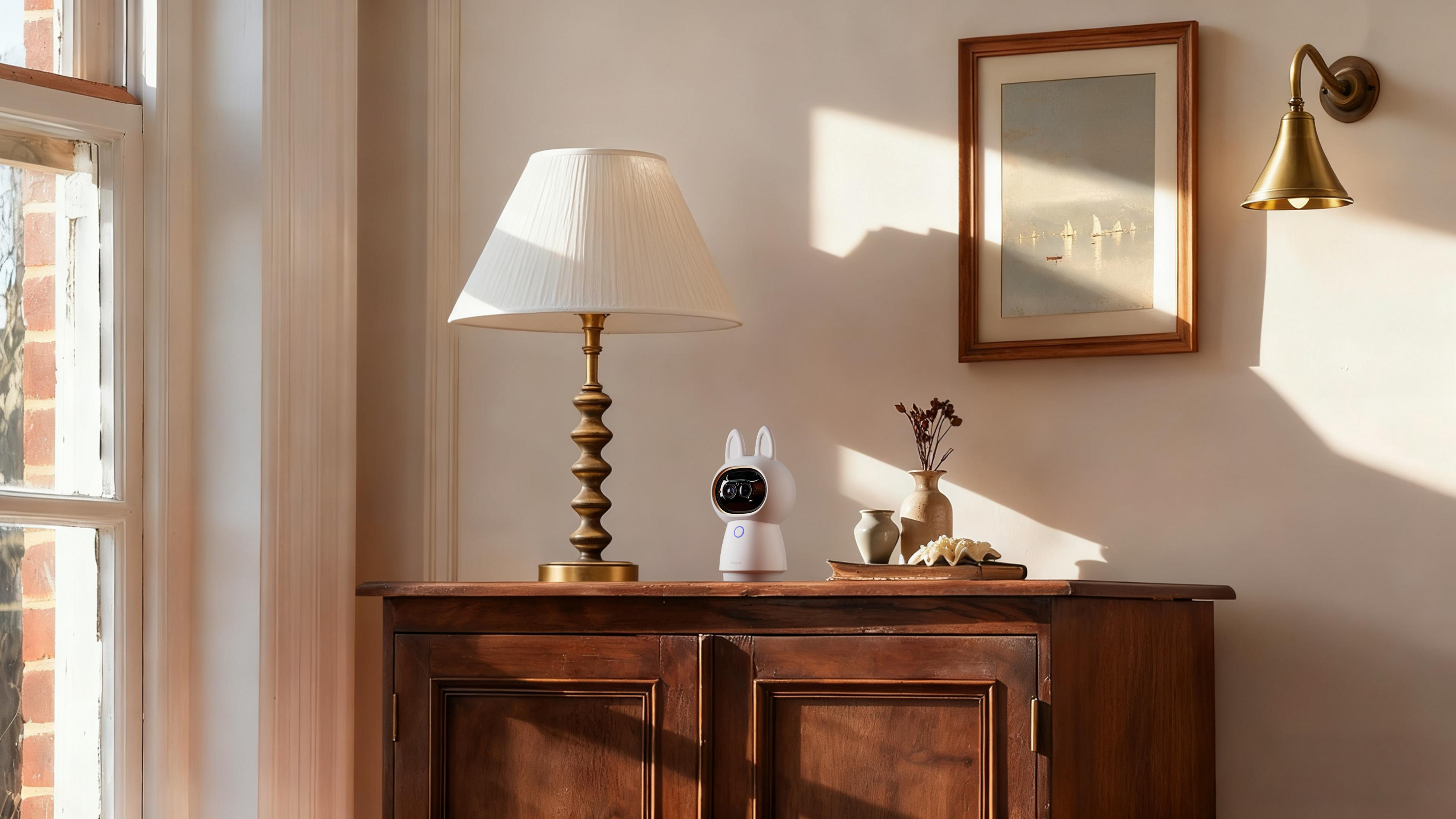 Ein weißer Roboter mit Katzenohren steht auf einem Holzschrank neben einer Lampe.