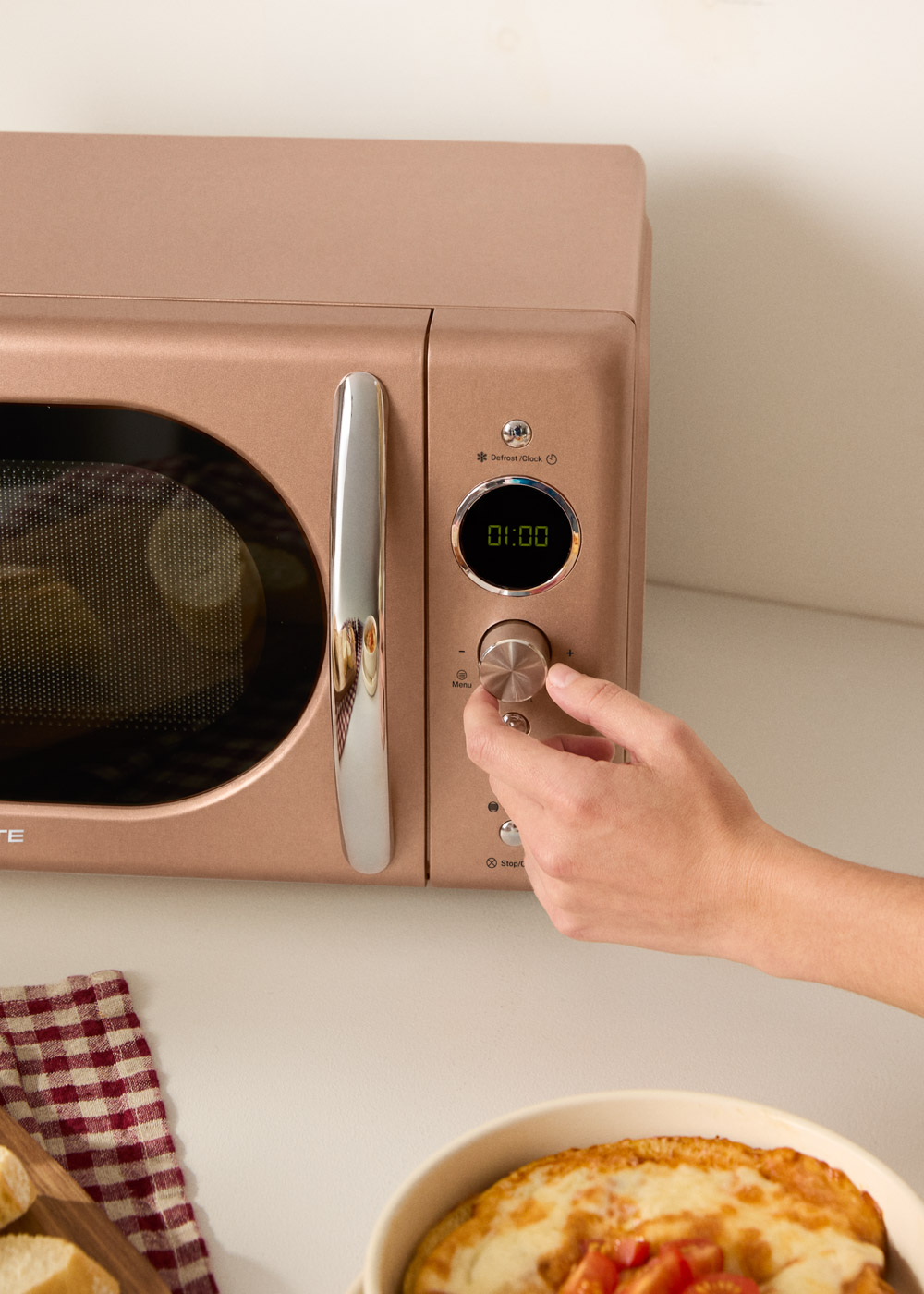 Una mano gira un dial en un microondas oro rosa con pantalla digital.