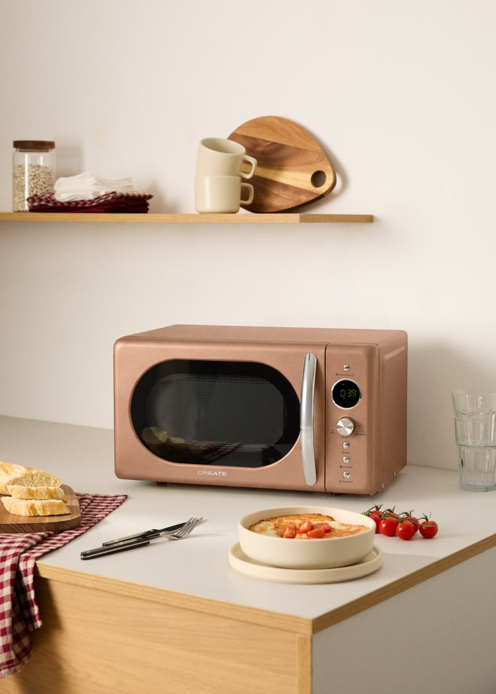 Un microondas color oro rosa con jarra, tazas, tabla de cortar y comida.