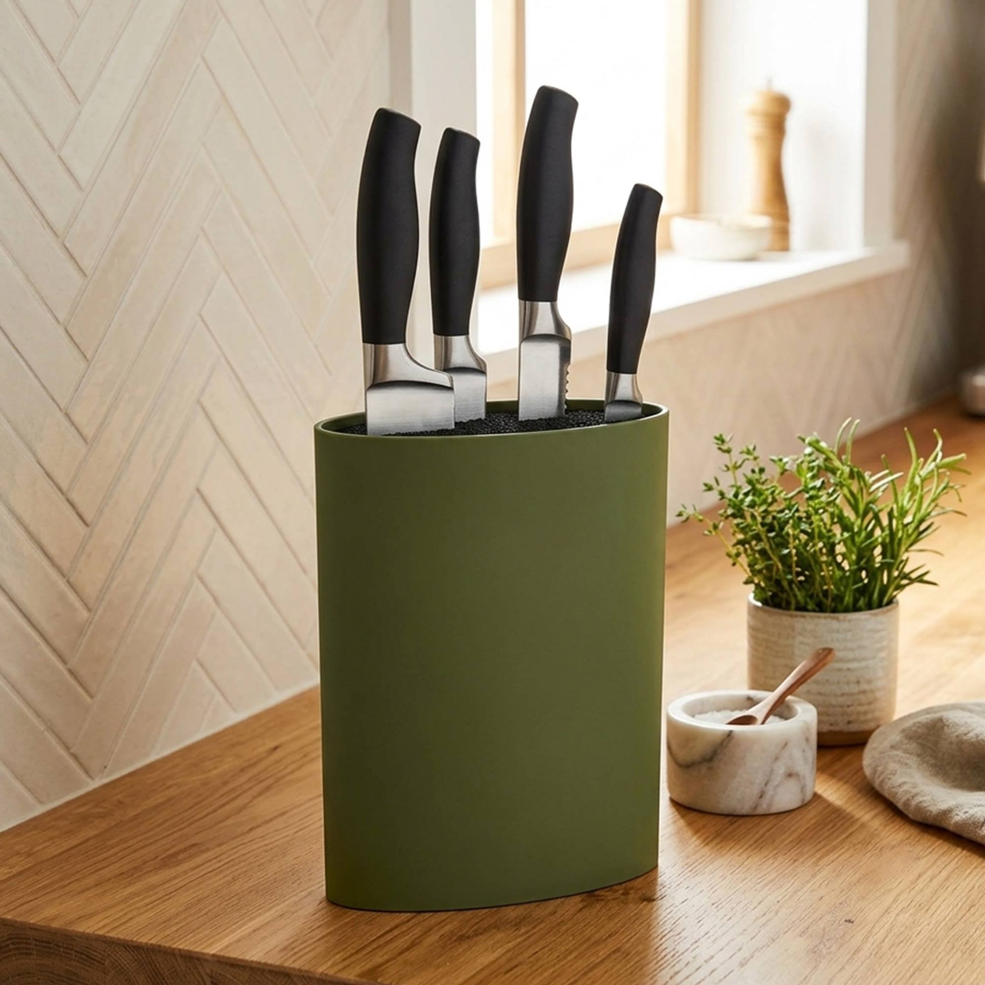 Un bloque de cuchillos de plástico verde con cuatro cuchillos, junto a una maceta de hierbas.