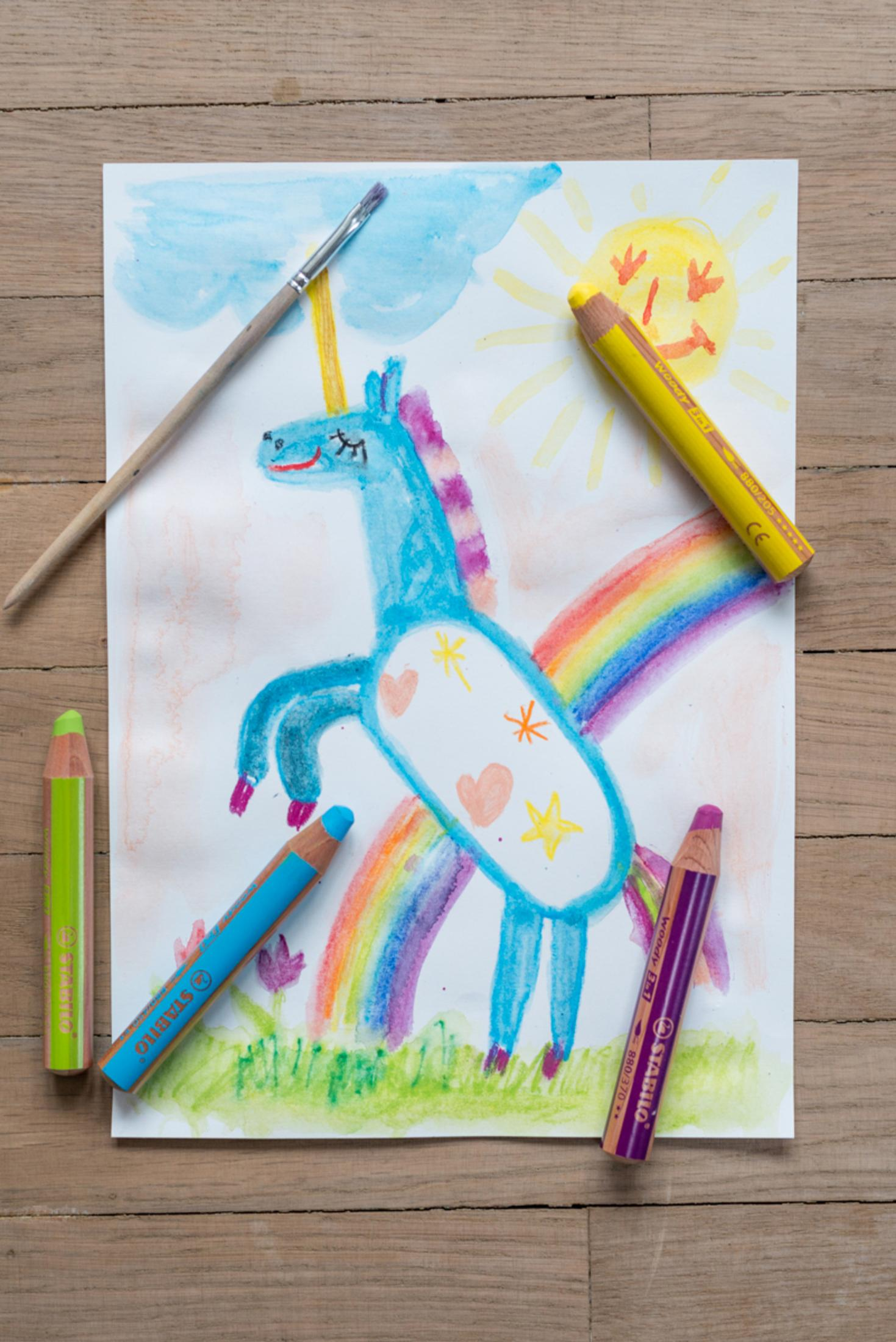 Buntes Bild eines Einhorns mit Regenbogen, Sonne und Wolken, umgeben von Buntstiften.