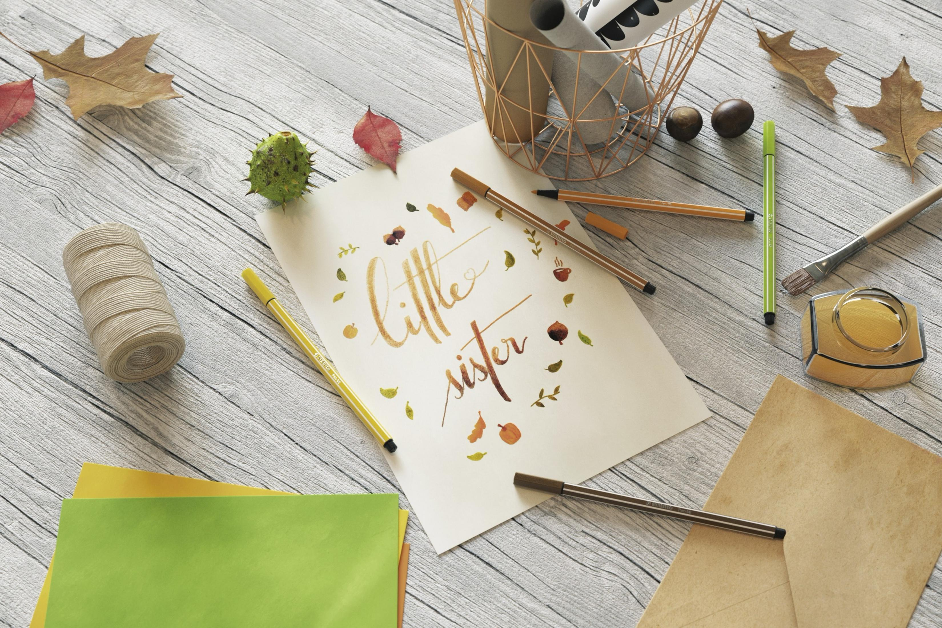 Schreibwaren und Herbstdekoration auf Holz, mit Schriftzug 'little sister'.