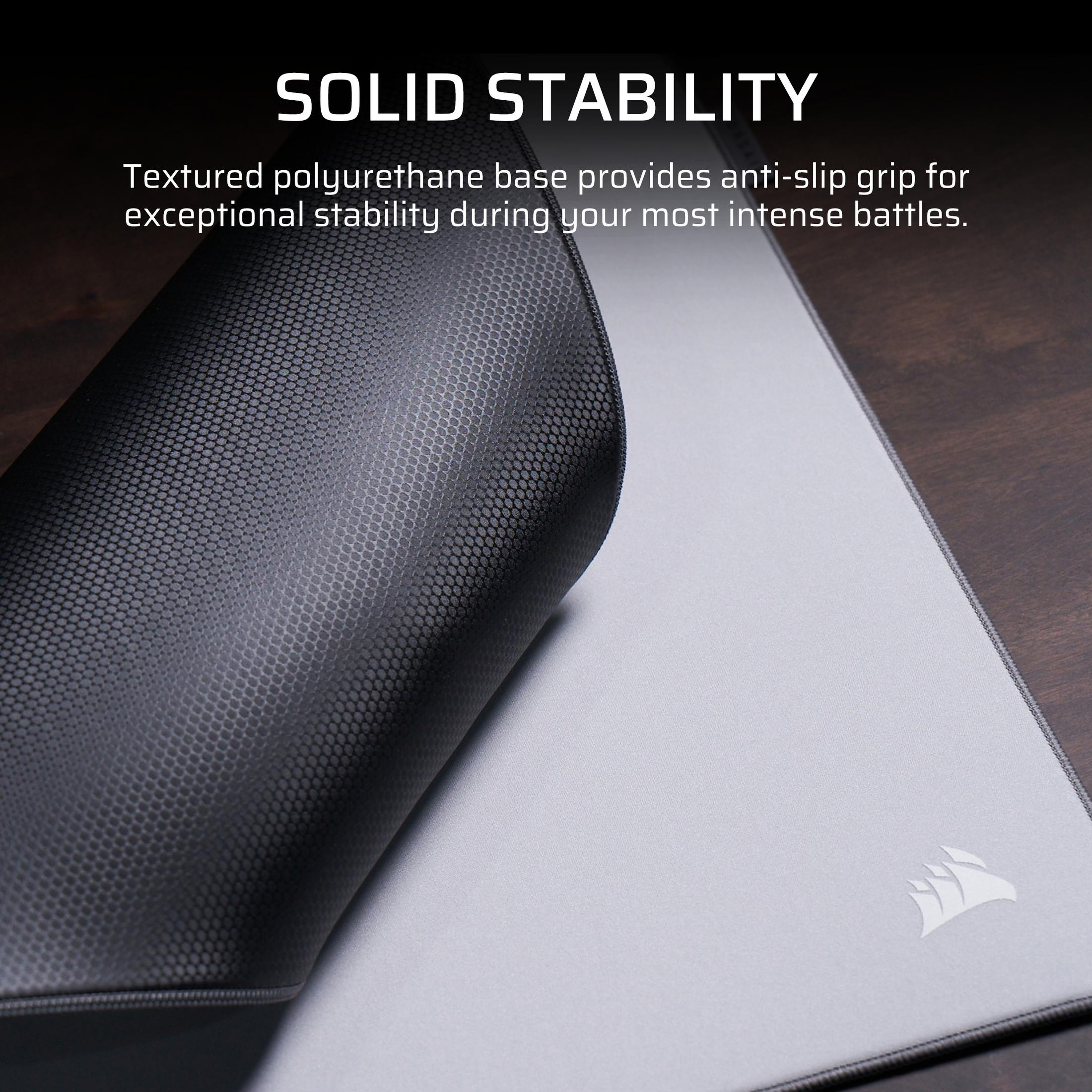 Graue Mousepad-Oberfläche mit aufgerolltem Rand, der schwarze, texturierte Unterseite zeigt.