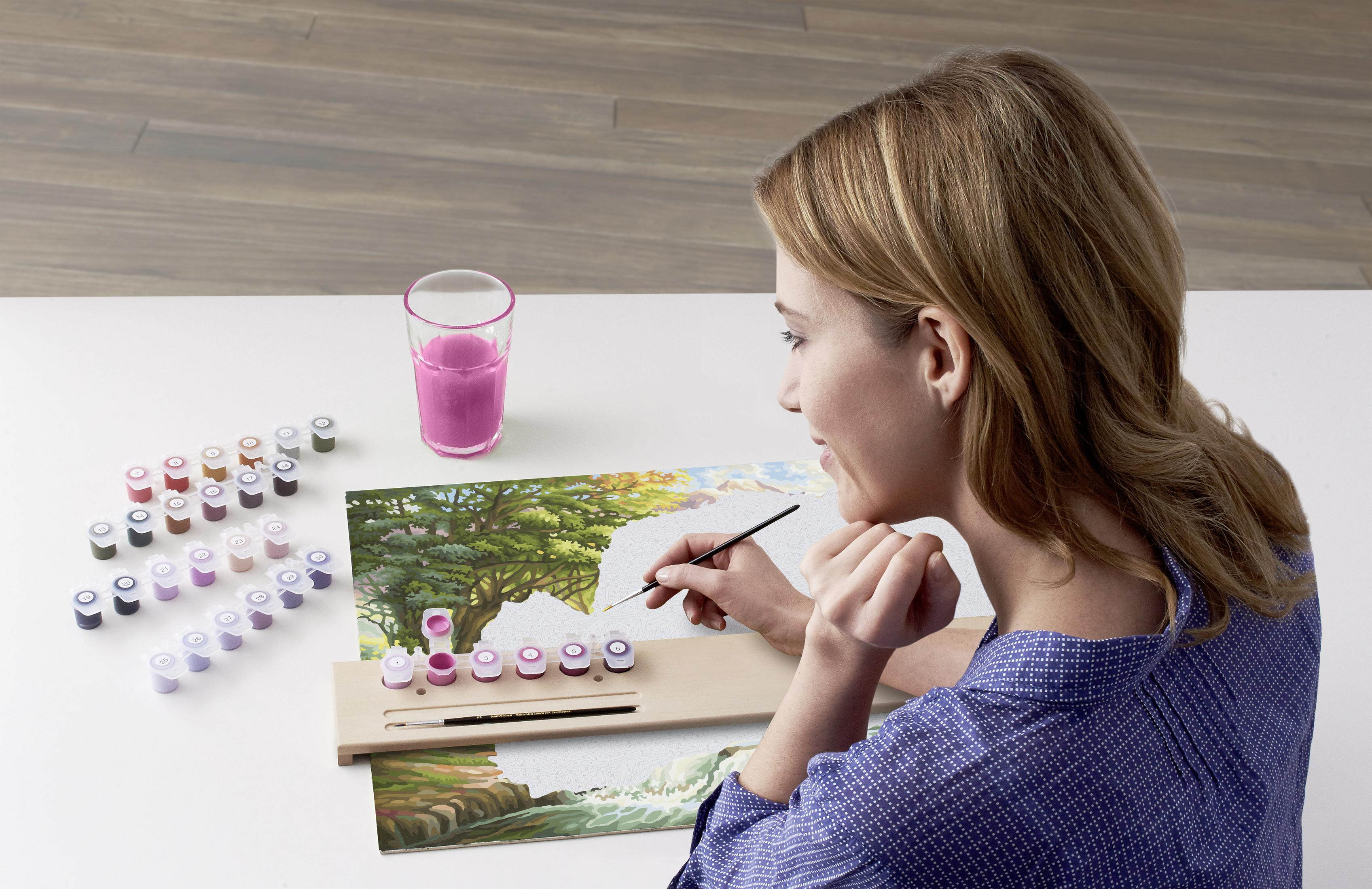 Frau malt auf Leinwand mit nummerierten Farben und Pinsel. Glas mit pinker Flüssigkeit.