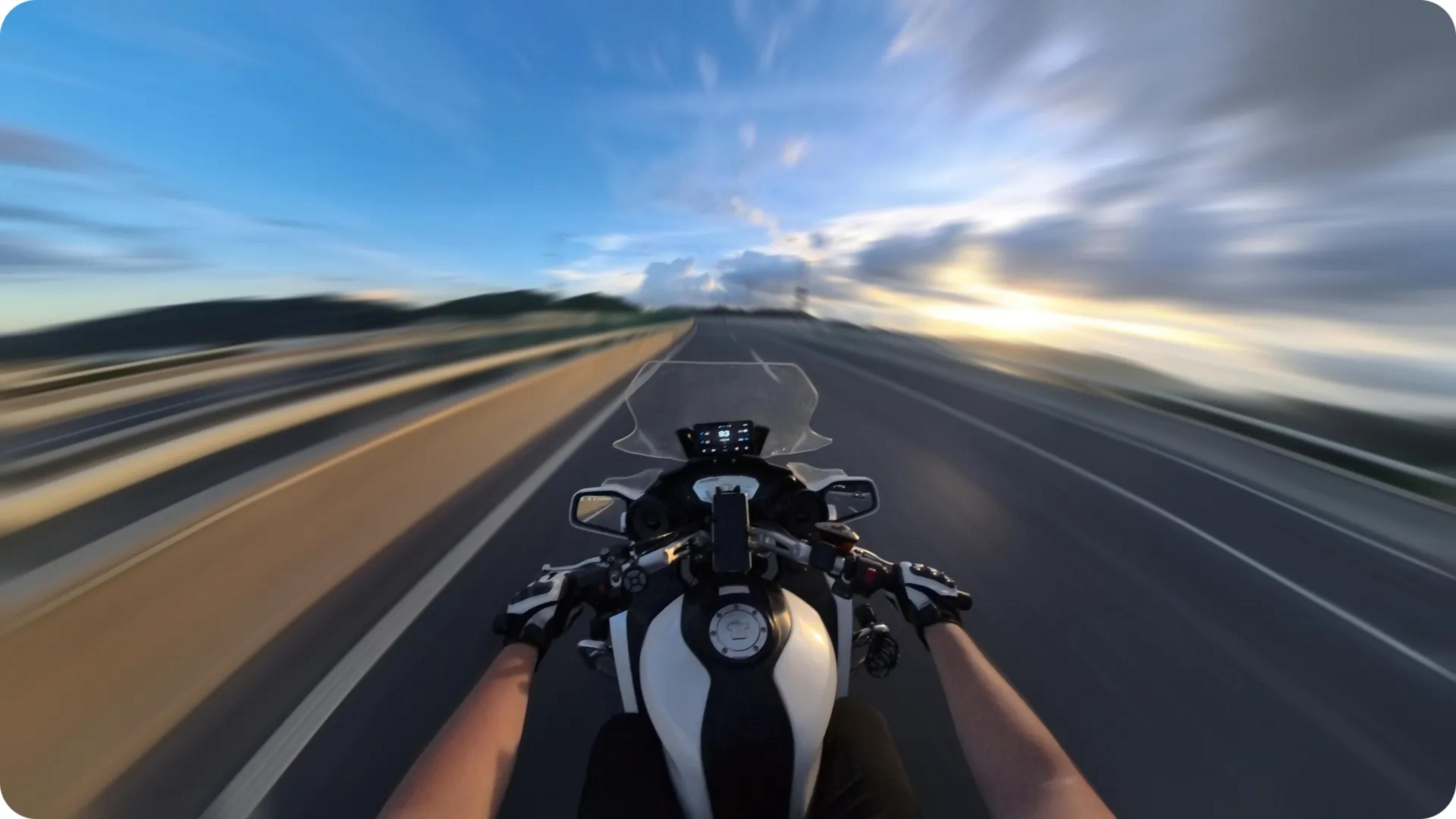 Motorradfahrer fährt auf einer Autobahn bei Sonnenuntergang, Himmel ist blau mit Wolken.