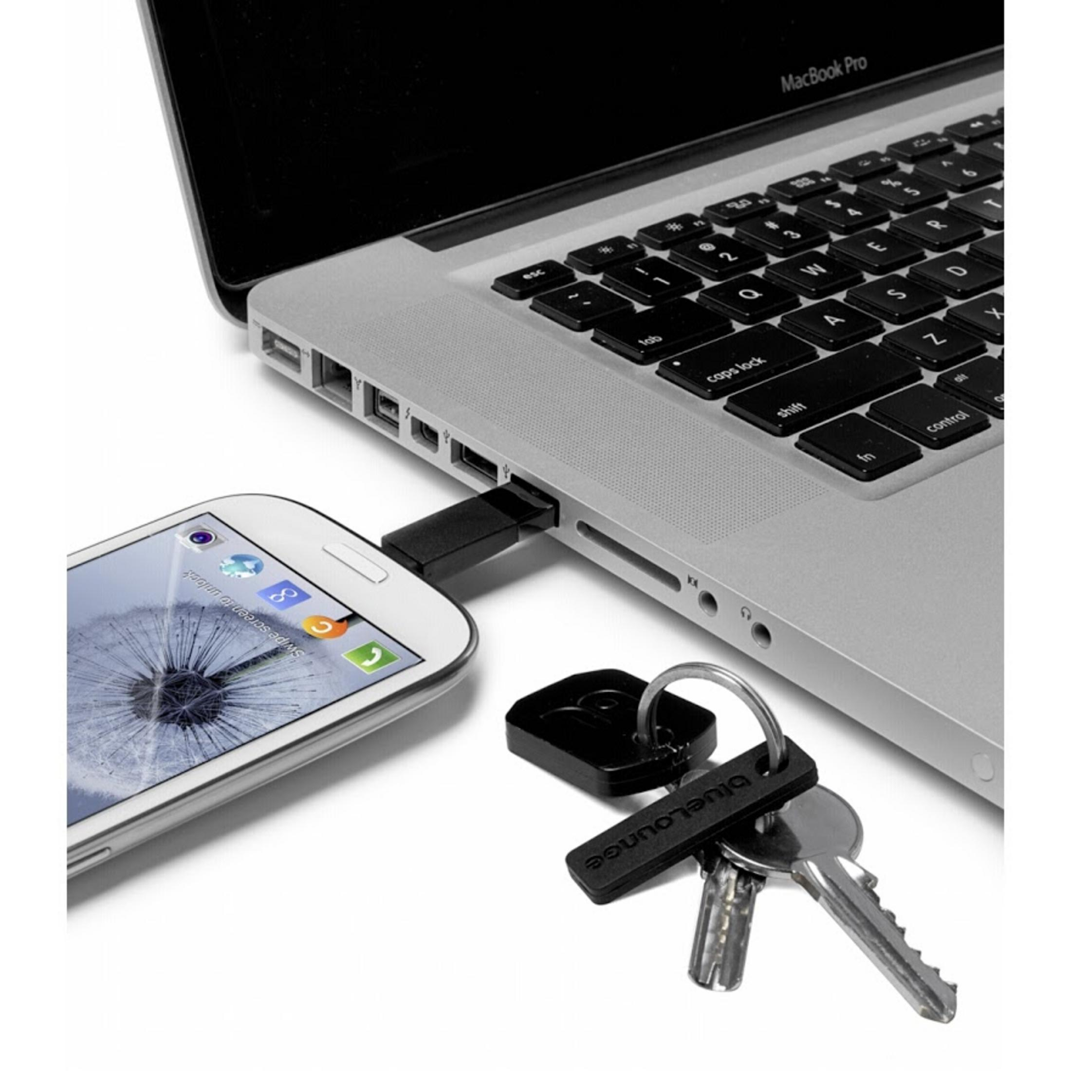 Ein MacBook Pro ist über einen USB-Stick mit einem Smartphone verbunden. Schlüssel sind in der Nähe.