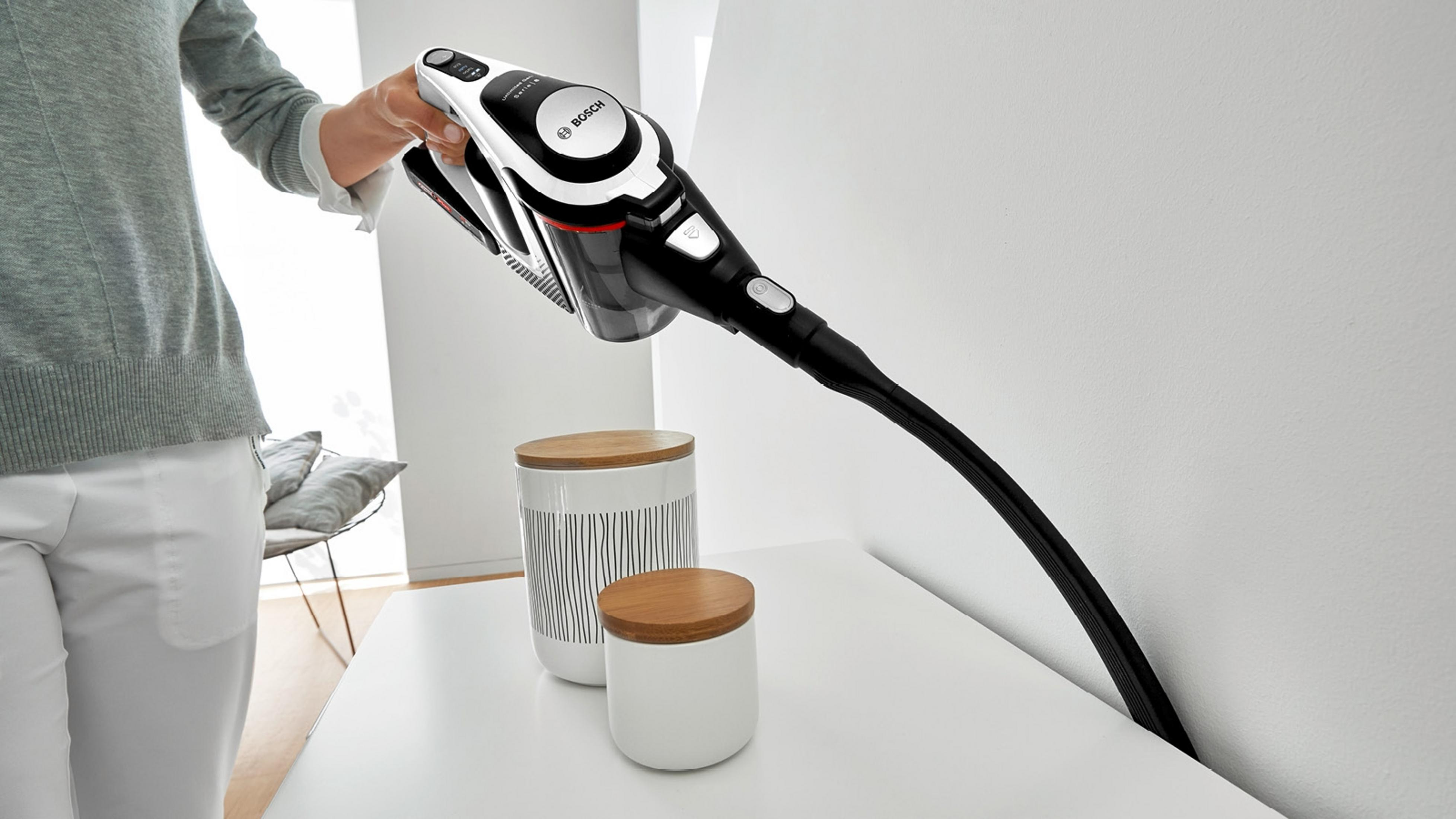Eine Hand hält einen schwarzen und weißen Bosch-Staubsauger über zwei Behältern.